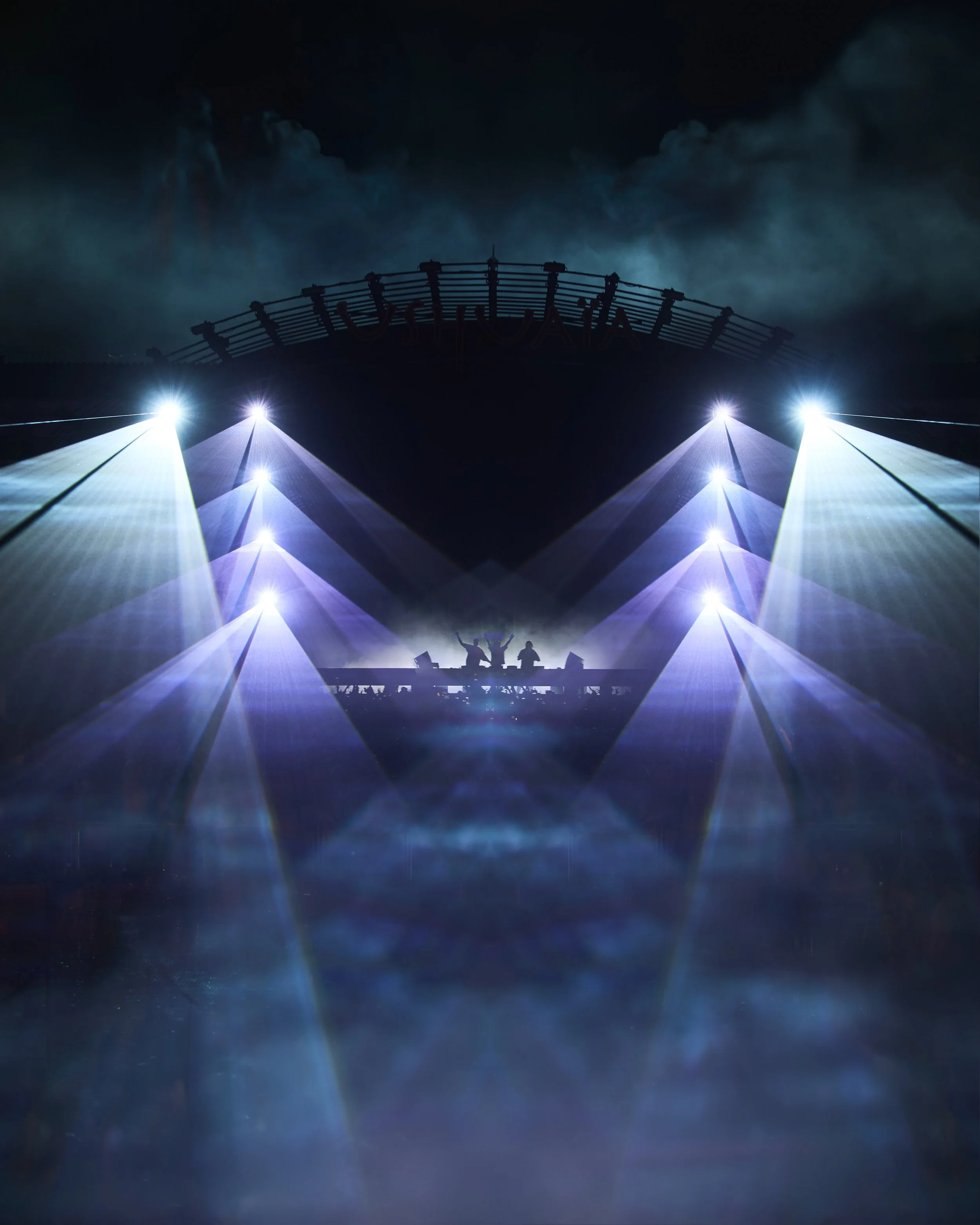 Dark night sky with clouds and bright lights illuminating a large tent structure with people inside, and a sign saying 'Ushuaia
' in the background.