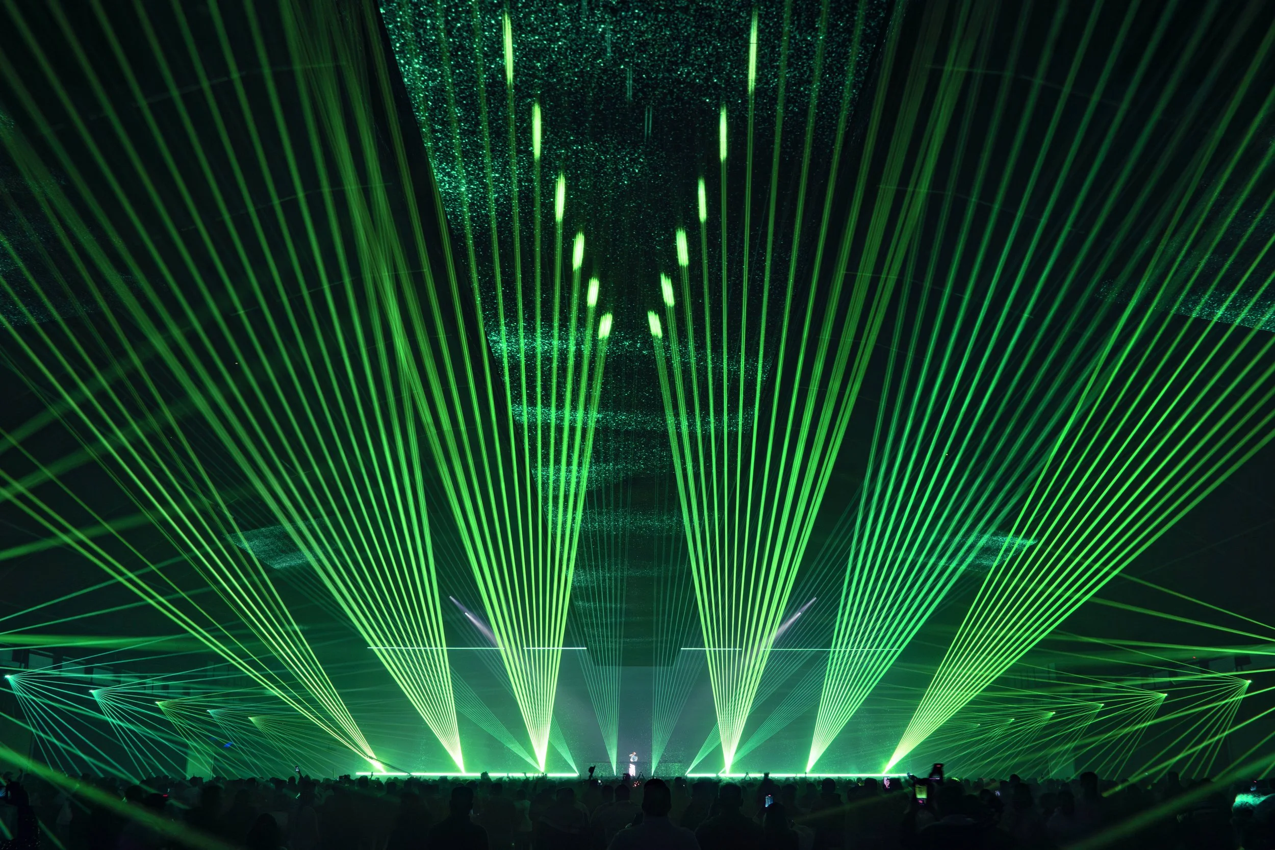 Green laser lights projected in a concert or event, with silhouettes of the audience in the dark.