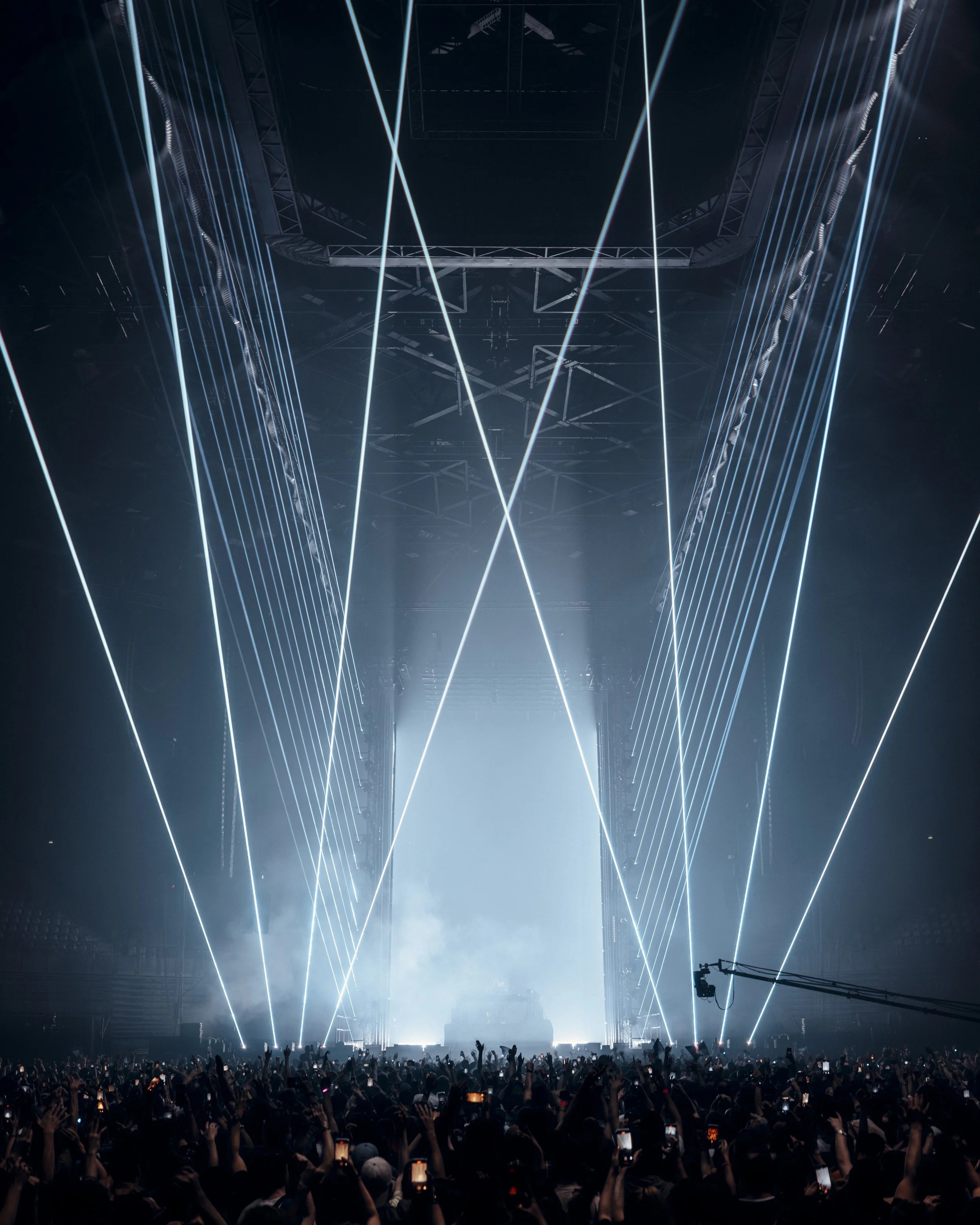 A large concert or music event with laser lights and a crowd of people holding their phones up, capturing the performance on stage.