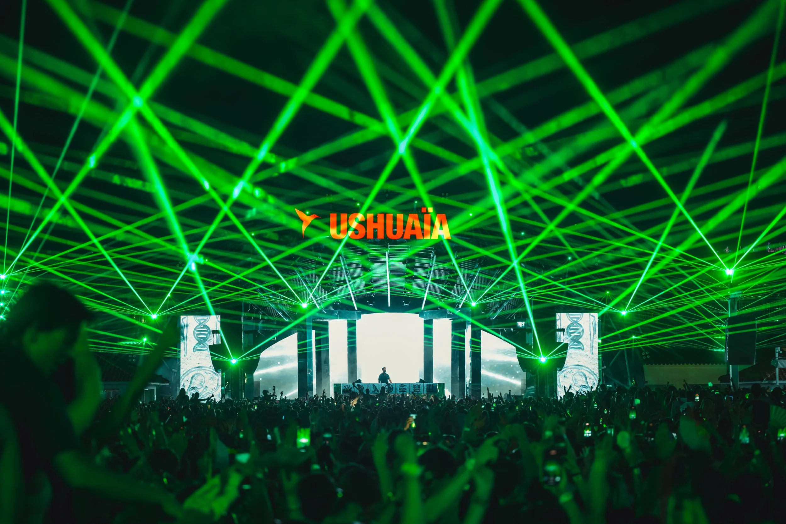 A large crowd at a concert or music festival with green laser light effects and a stage featuring Ushuaïa branding.
