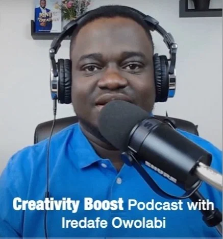 A man wearing a blue shirt with headphones speaking into a microphone, with a background showing shelves and framed pictures. The text overlay reads 'Creativity Boost Podcast with Iredafe Owolabi'.