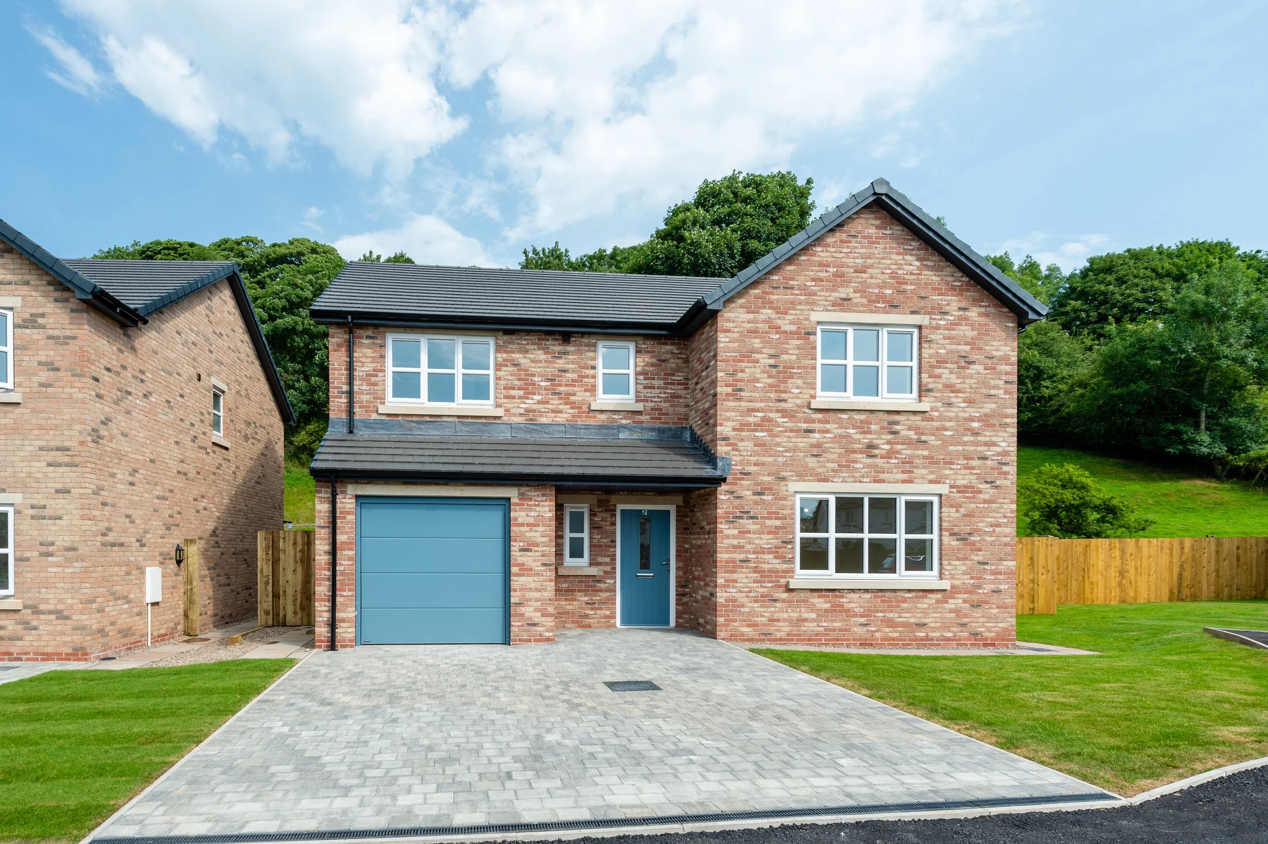 Newly built two-story brick house with a blue garage door and matching front door, green lawn, and paved driveway under a blue sky with clouds.