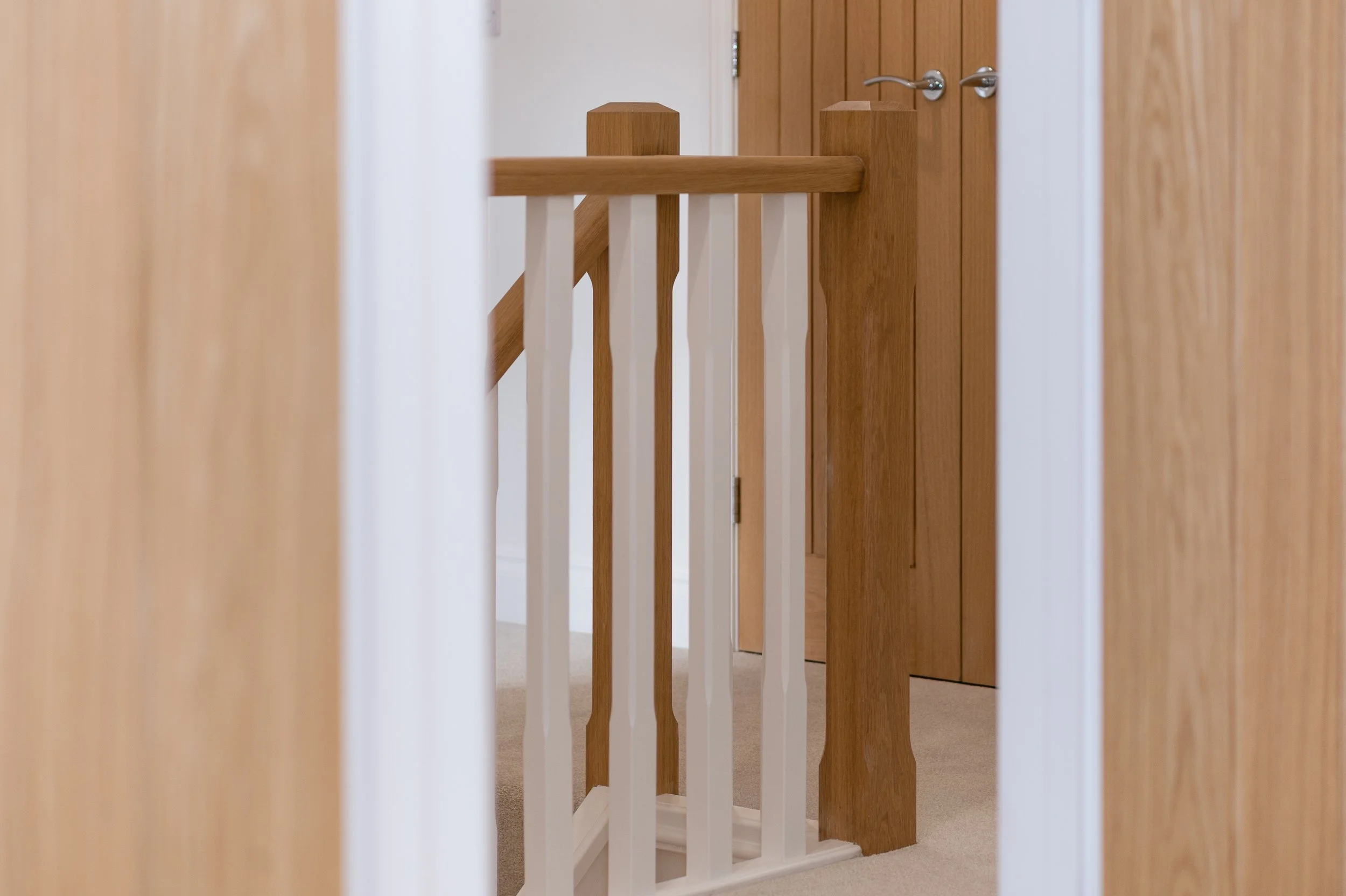 View of a wooden staircase and railing from a hallway with a closed wooden door.