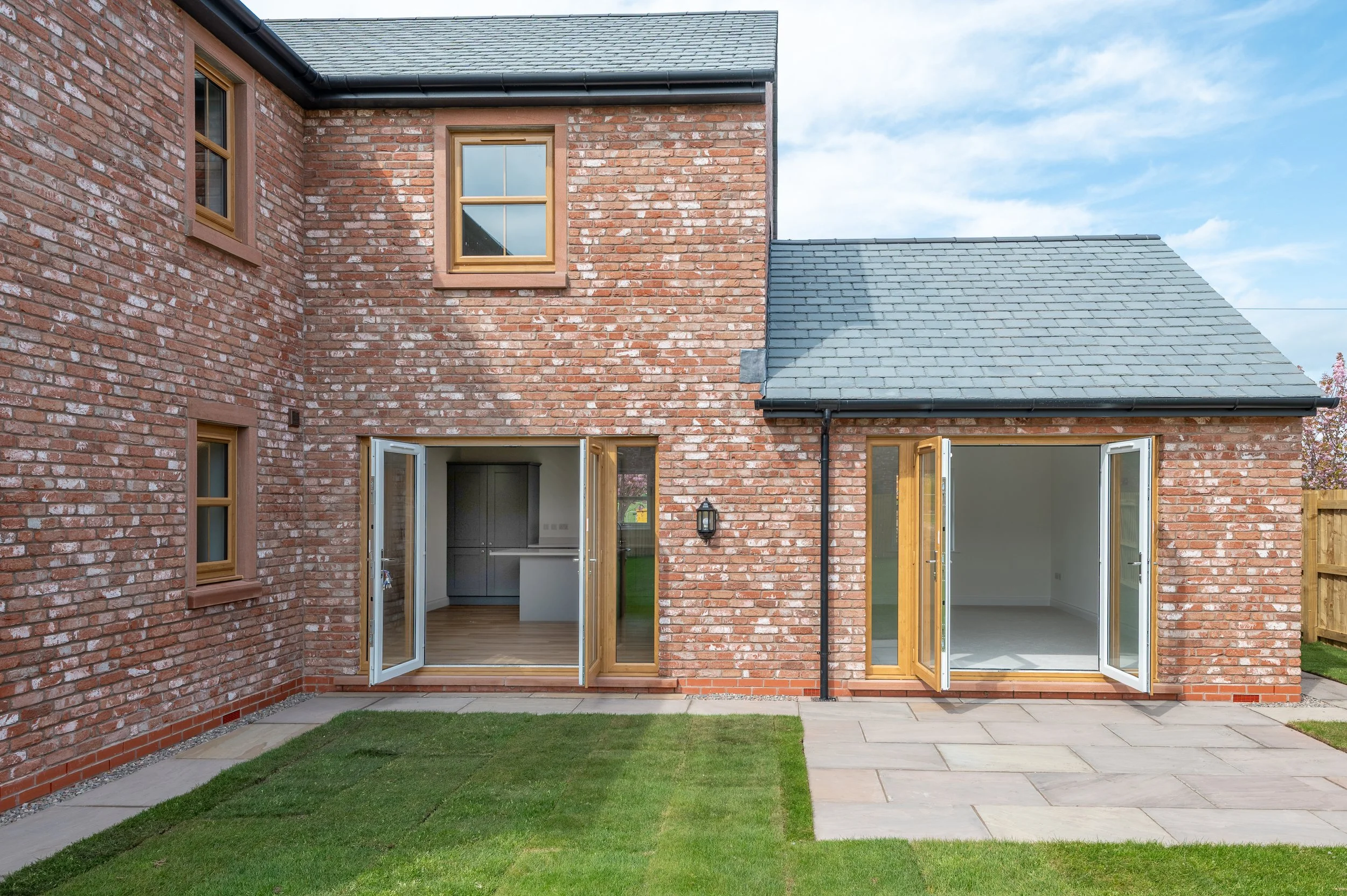 Backyard view of a brick house with open French doors leading to a patio and a green lawn.