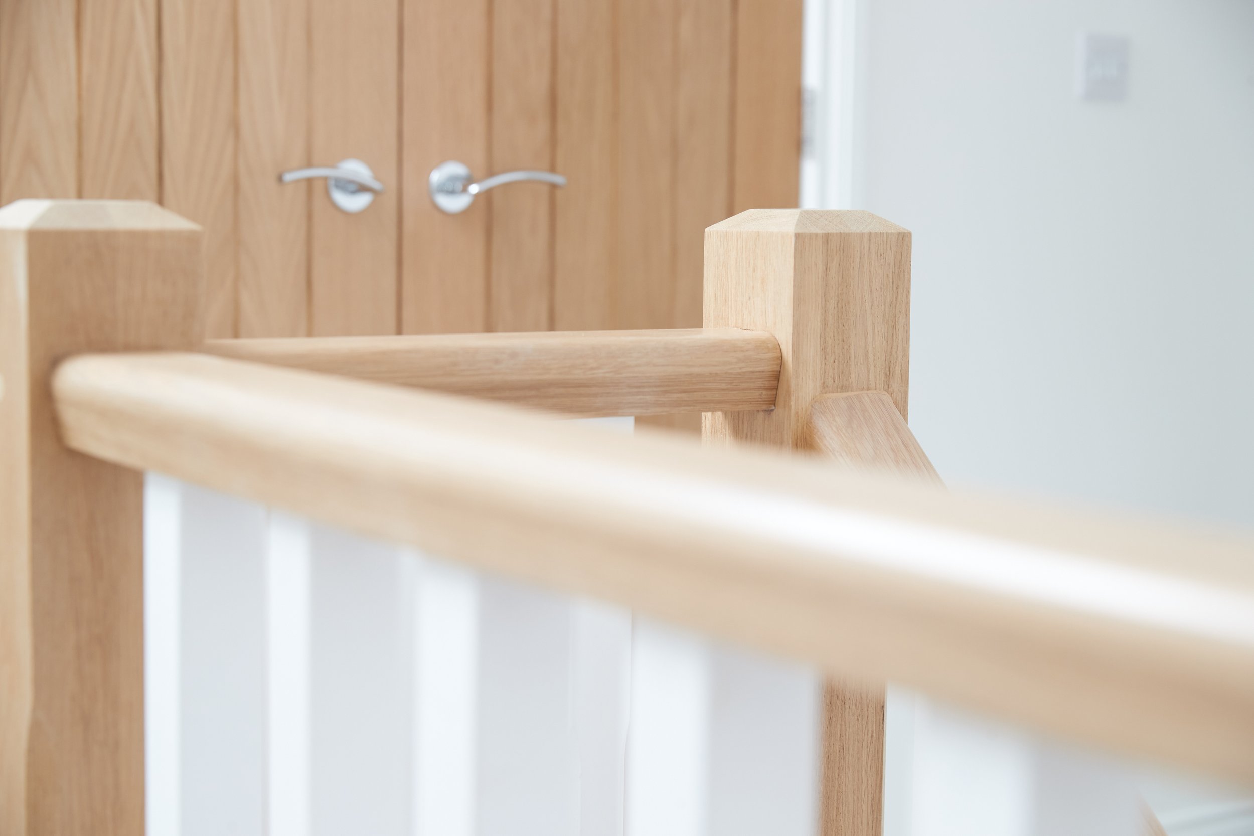Close-up of a light wood handrail and balusters on a staircase, with a wooden door and door handles in the background.