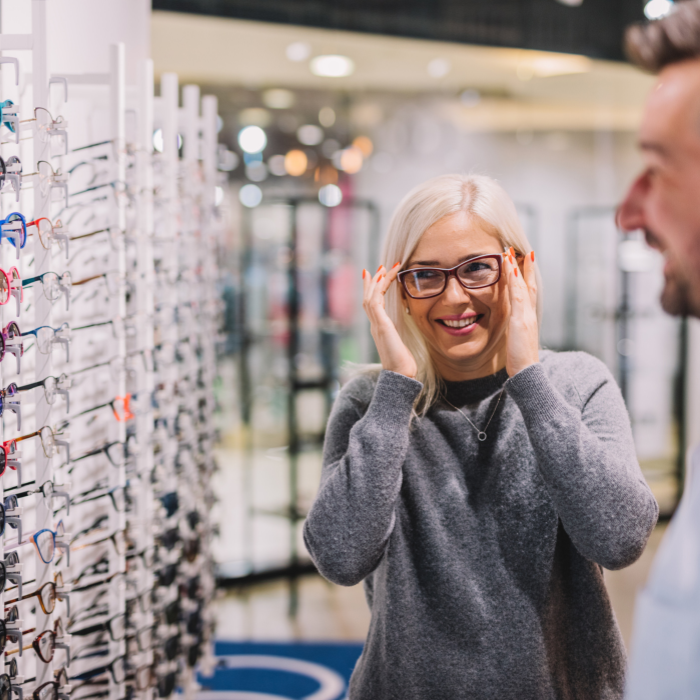Woman trying on glasses in an optical store, smiling at her reflection.