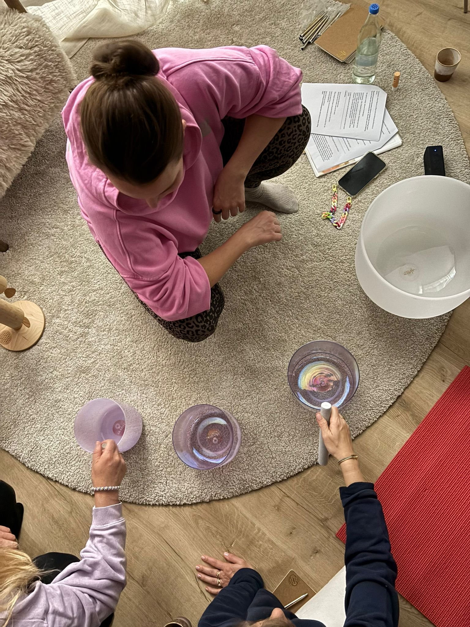 Menschen, die auf einem Teppich im Raum Yoga- oder Meditationskristalle halten, während weitere Personen und persönliche Gegenstände im Hintergrund sichtbar sind.