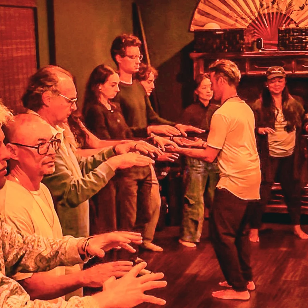 People participating in a synchronized hand-exercise or activity in a cozy, warmly-lit room with Asian decor elements.