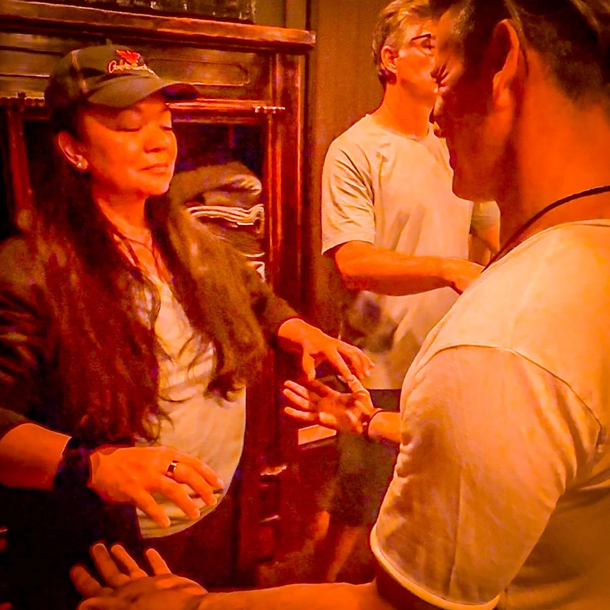 Several people engaged in a conversation indoors, with one woman wearing a cap, another person in glasses, and two others partially visible.