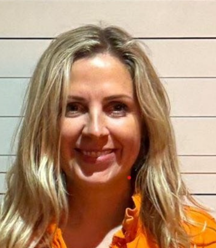 Head and shoulders of Emma Oliver-Taylor wearing an orange top in front of a white background with horizontal black lines