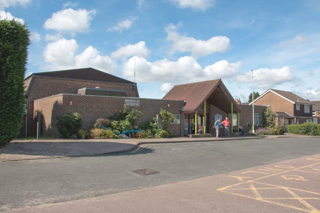 The exterior of the Henfield Hall and Museum with a few people standing outside on a sunny day.
