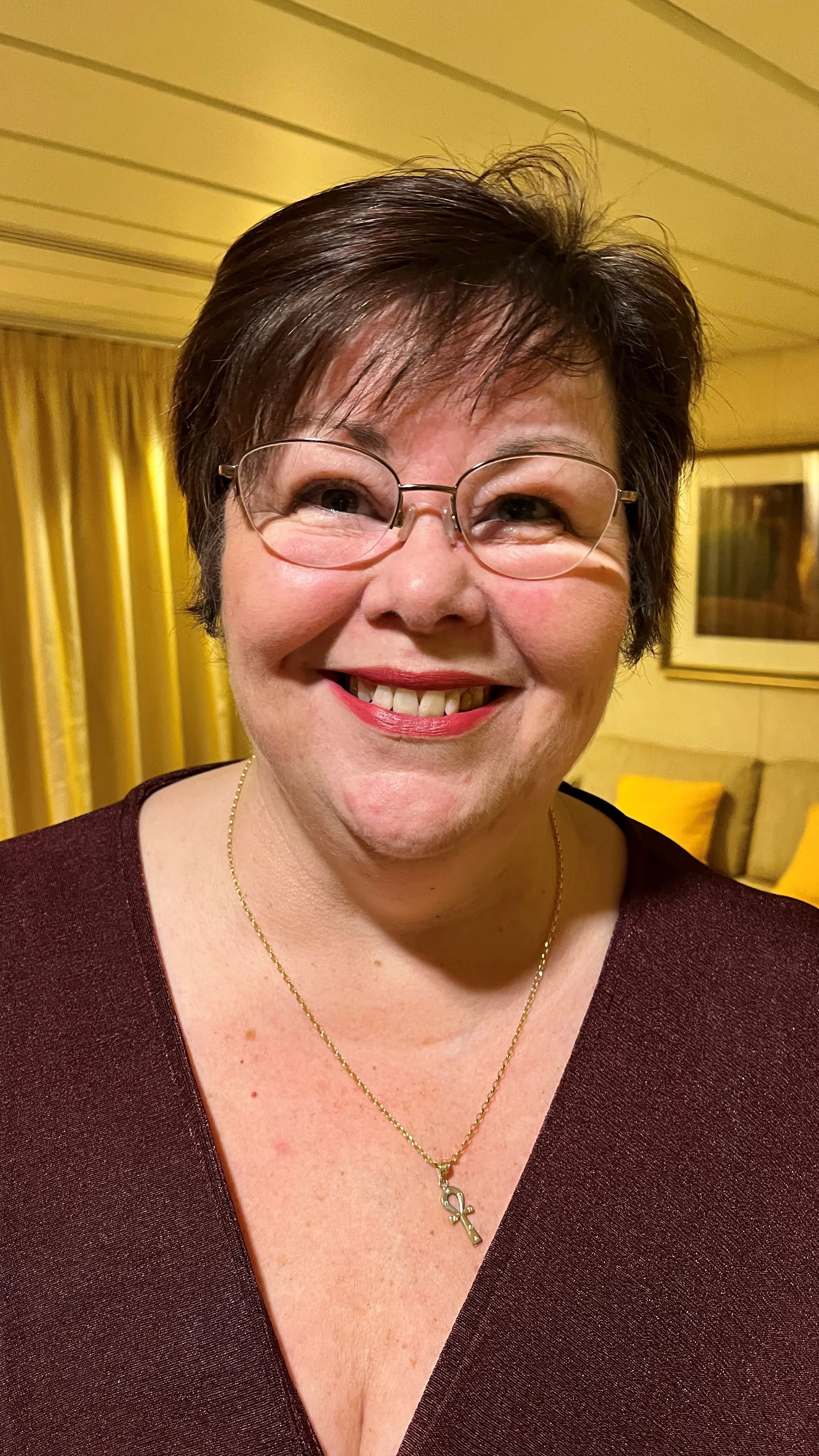 Head and shoulders of Dawn Butchers wearing a v neck top in a yellow room.