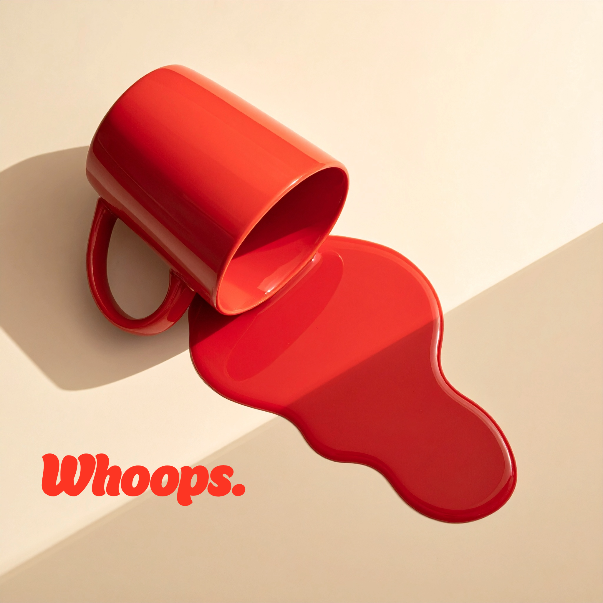 A red mug tipped over spilling red liquid onto a white surface with the word "Whoops." in red text.