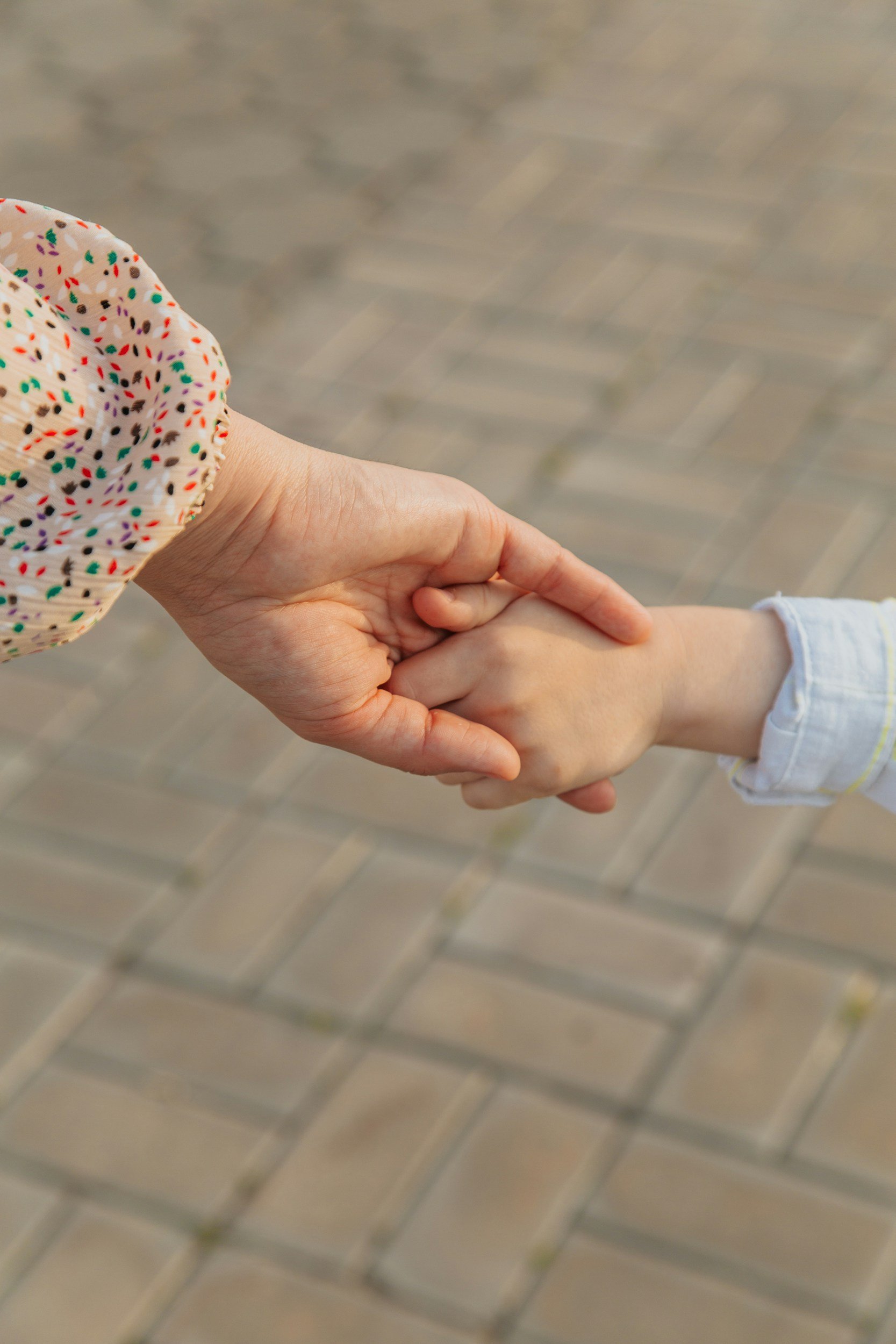 The Open Door - therapeutic practice. Counselling. Dyadic Developmental Psychotherapy (DDP)
 An adult and a child holding hands. The adult's hand is on top, and the child is holding onto the adult's hand. The background shows a paved surface.