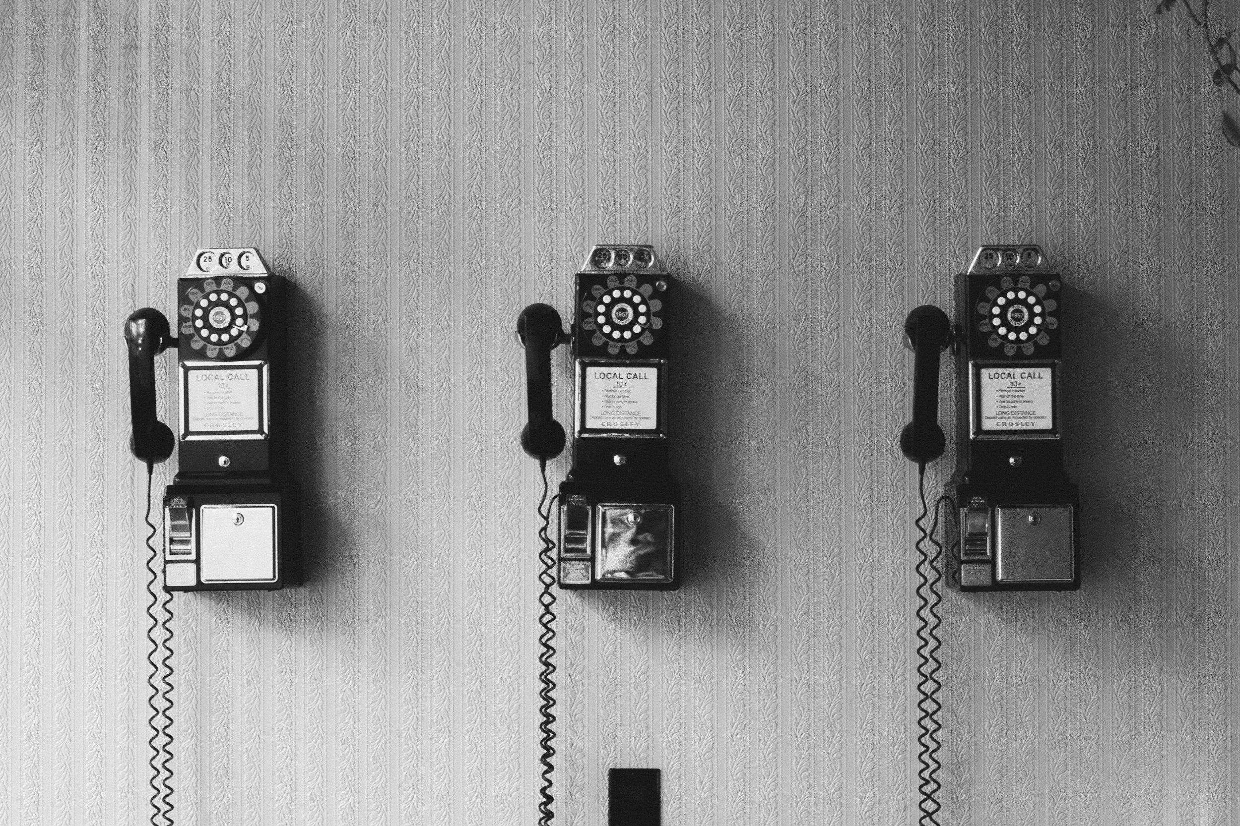 Three vintage rotary dial payphones on a textured wallpapered wall.