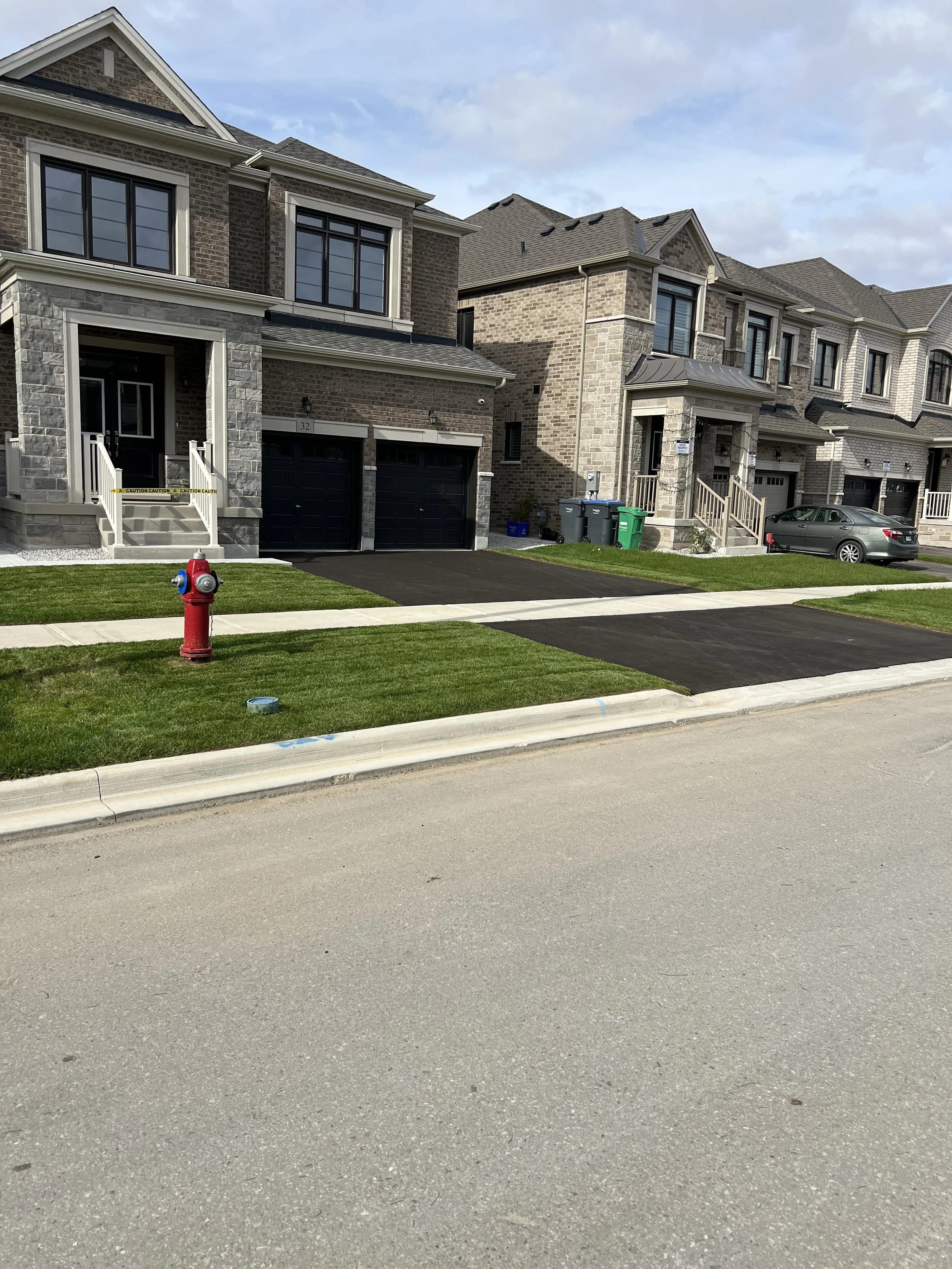 Recently constructed townhouse complex with attached garages, front porches, a fire hydrant, and newly paved parking areas, in a suburban neighborhood.