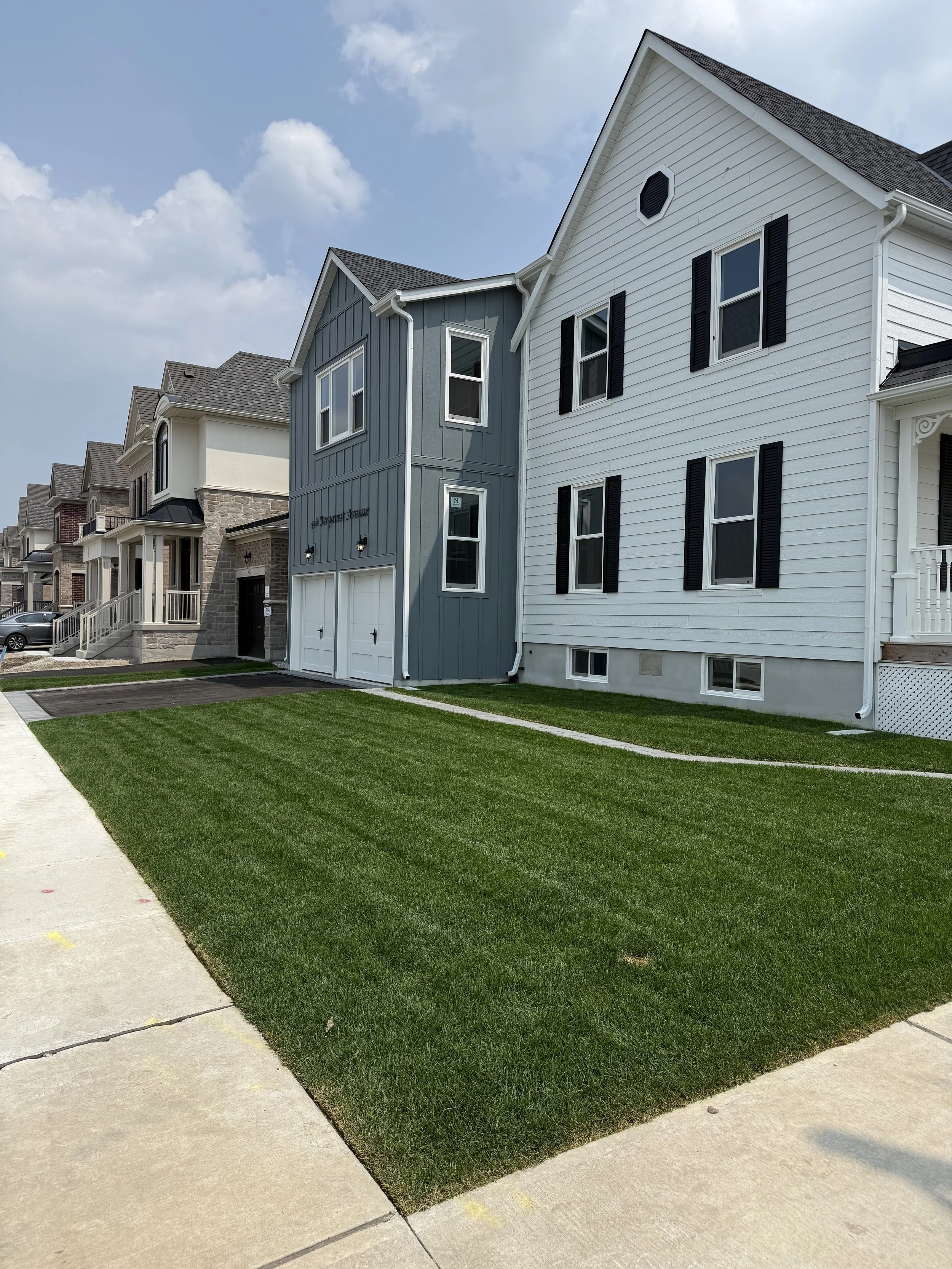 A row of modern suburban houses with well-maintained lawns and sidewalks in front.