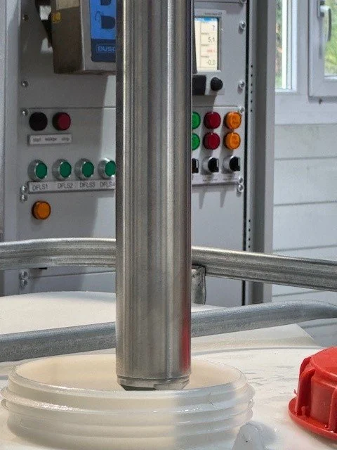 Industrielle Maschine mit Knöpfen und Steuerung, Abfüllanlage in einer  Produktionshalle, mit einem weissen Behälter und einem roten Verschluss.