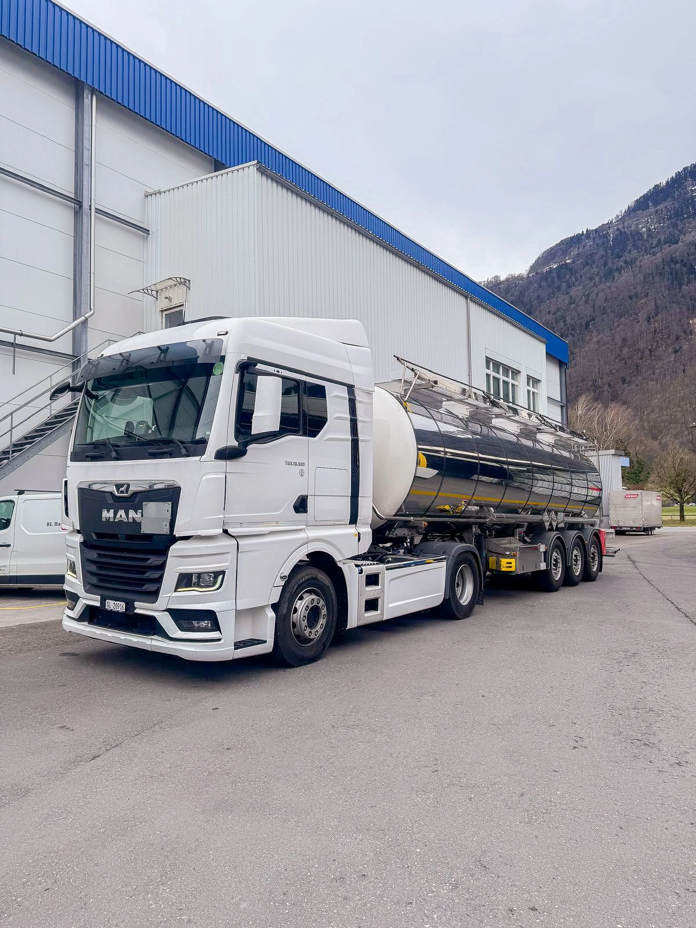 Ein weisser Tankwagen mit einem Tankanhänger ist vor einer Fabrikhalle parkiert.