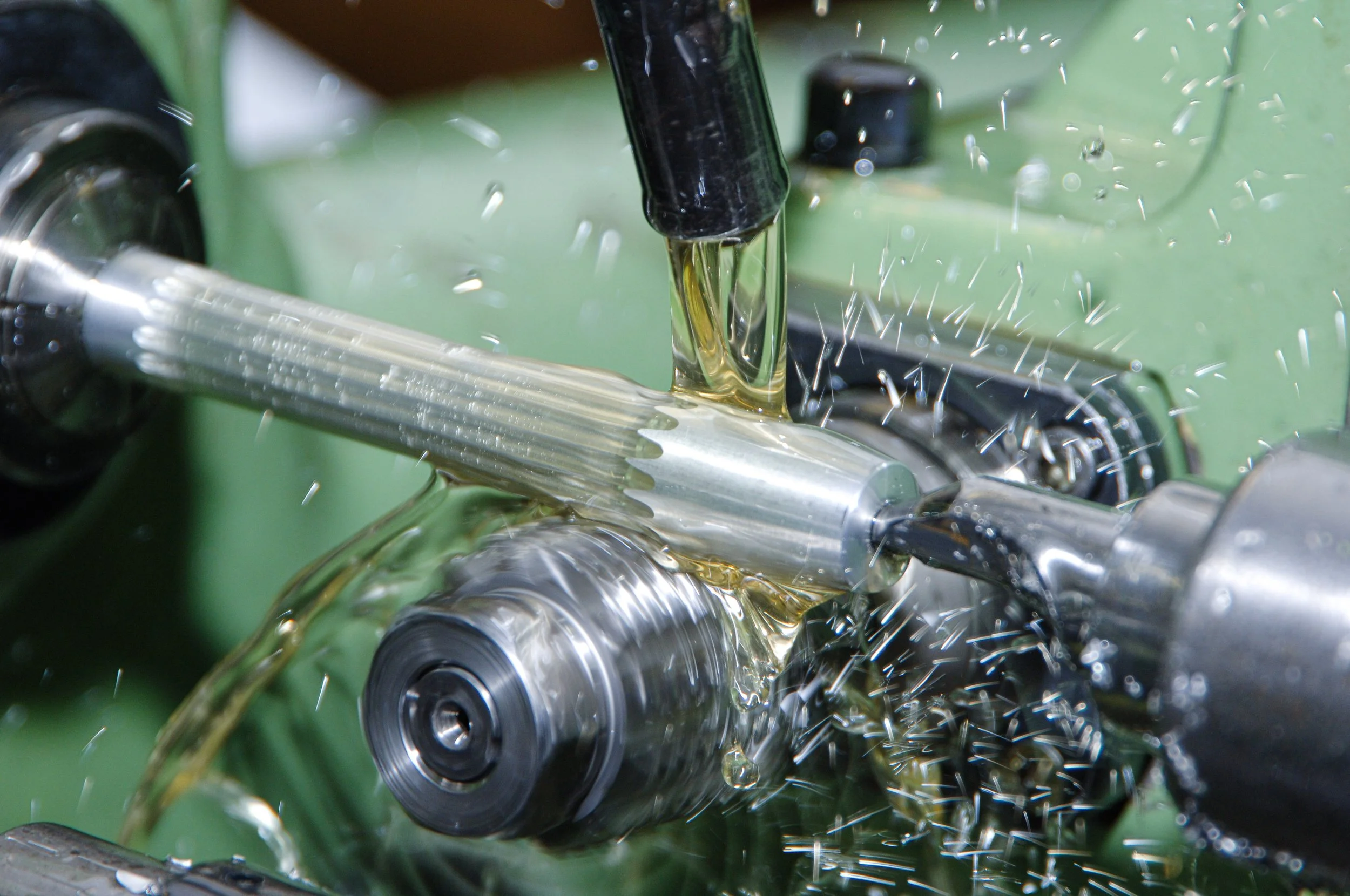 Fräser bearbeitet eine metallene Welle in einer Fertigungsmaschine, Wasser und Metallspäne fliegen bei der Bearbeitung herum.