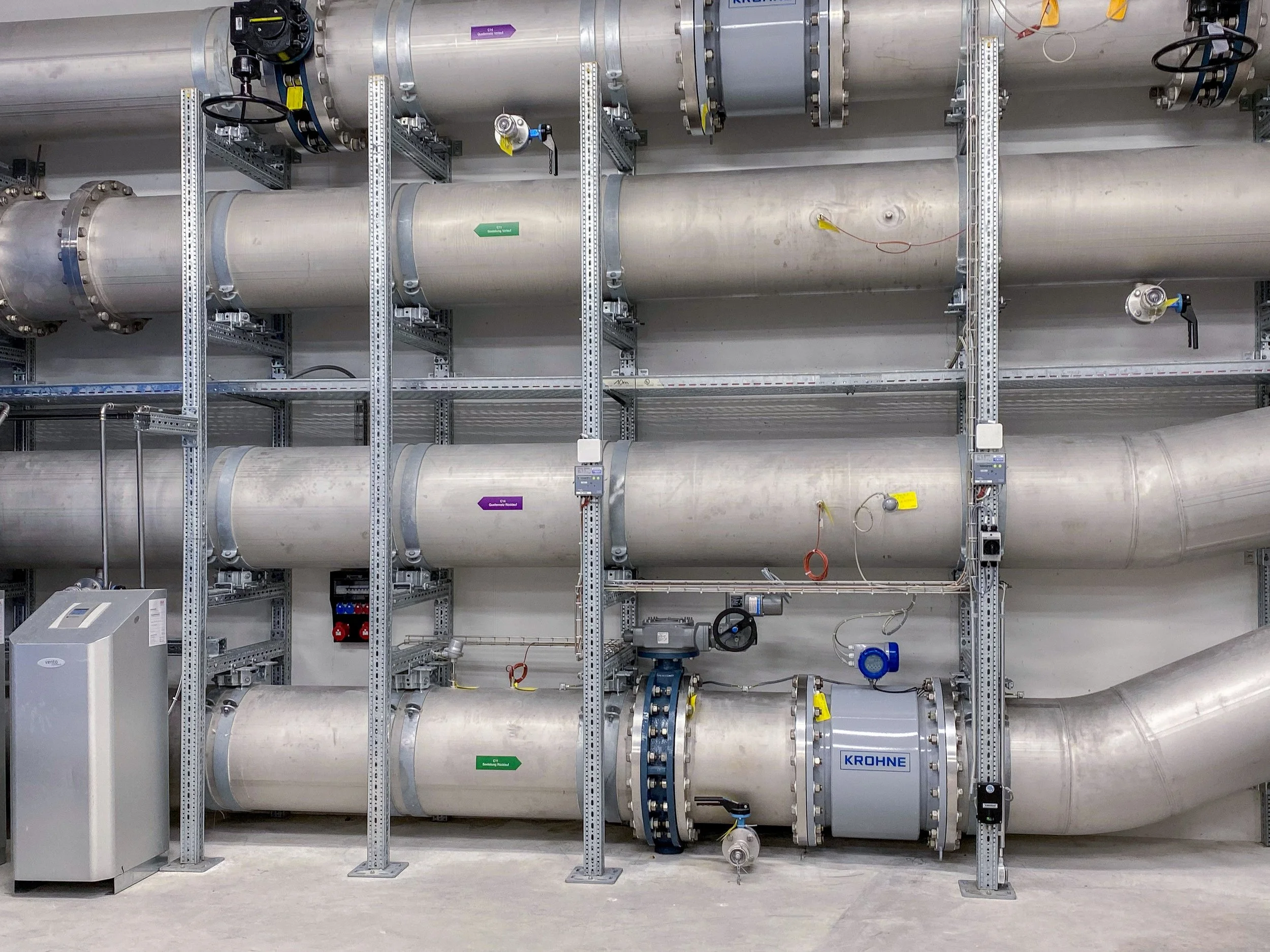 Grosse industrielle Rohrleitungen in einer technischen Anlage, mit mehreren Ventilen, Messgeräten und Schalttafeln.
