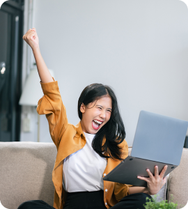 A woman sitting on a sofa, excited and celebrating while using a laptop.