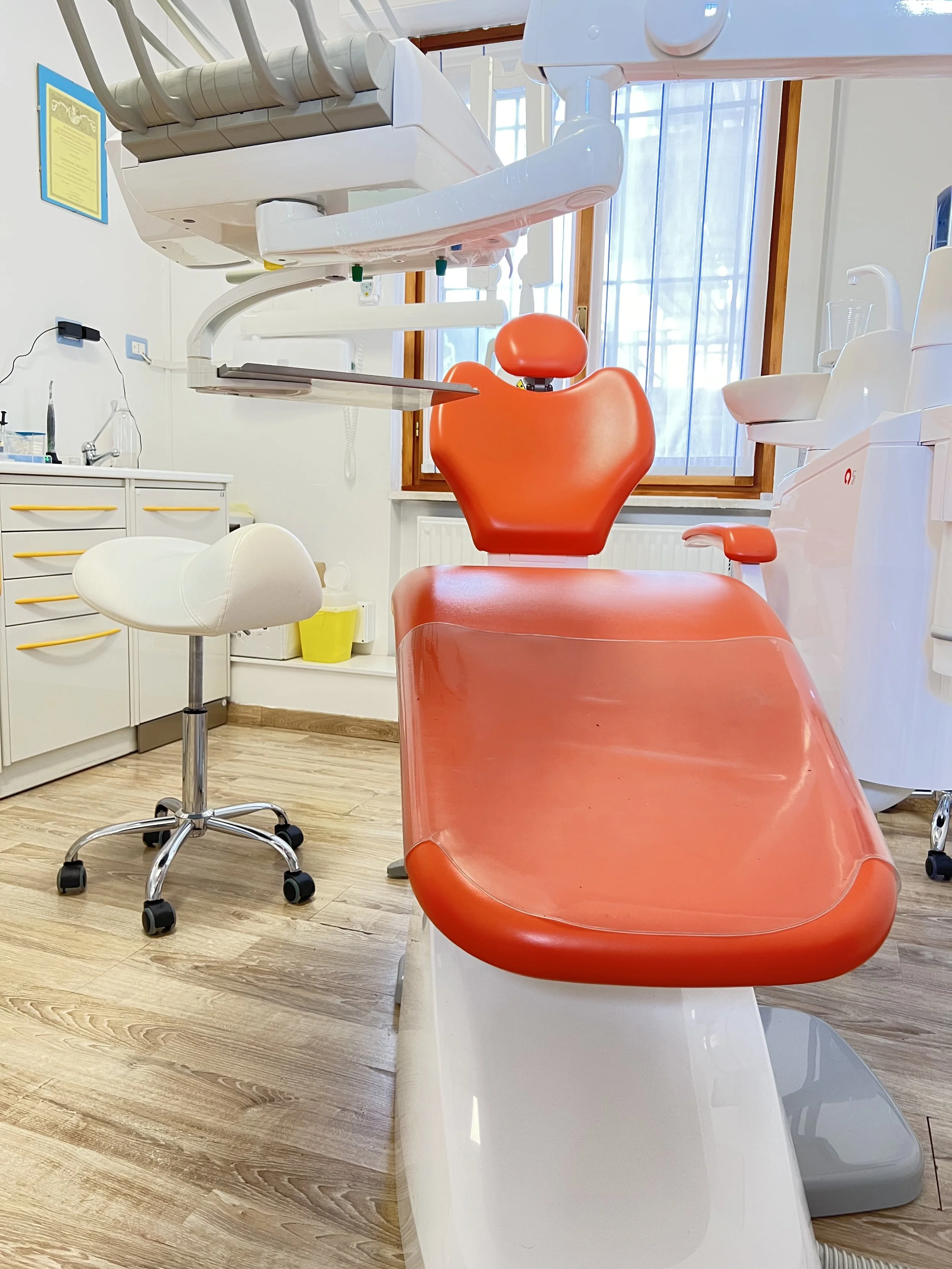 Poltrona odontoiatrica rosso arancione in uno studio dentistico, con attrezzature e sedia per il personale in secondo piano.