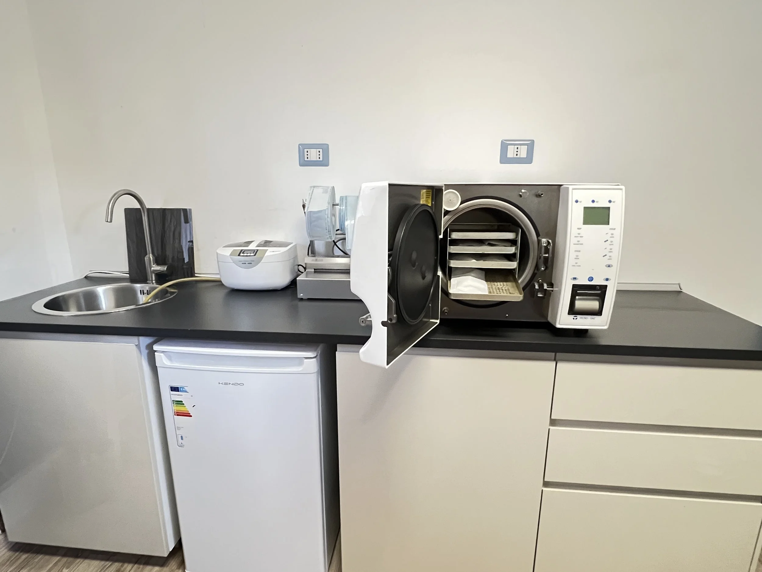 Zona di laboratorio o cucina con lavabo, microonde, forno a farinna subito, piccoli elettrodomestici e ripiani.