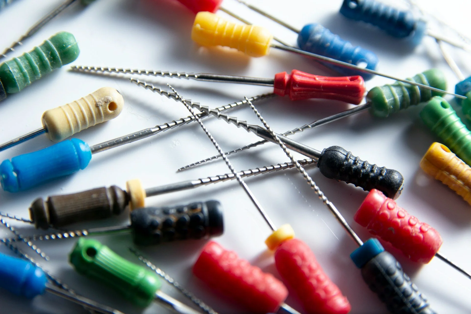 Numerosi filamenti colorati e punte di vari diametri disposti casualmente su una superficie bianca.