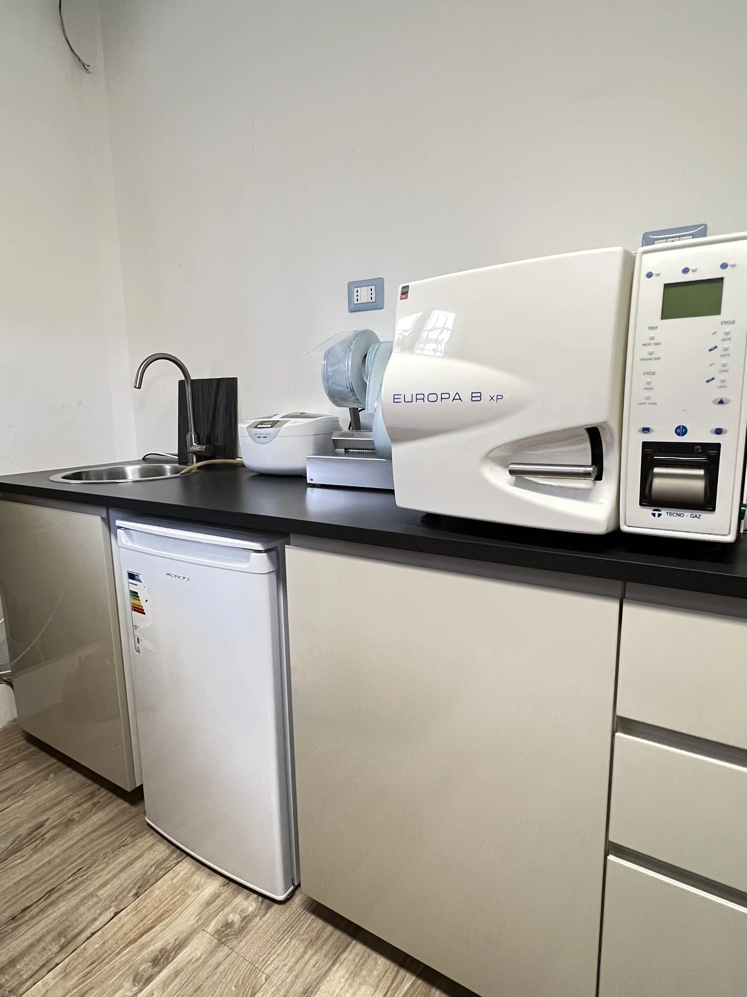 Angolo di una cucina con un lavandino, una piccola frigorifero, un forno a raggi UV e altri apparecchi