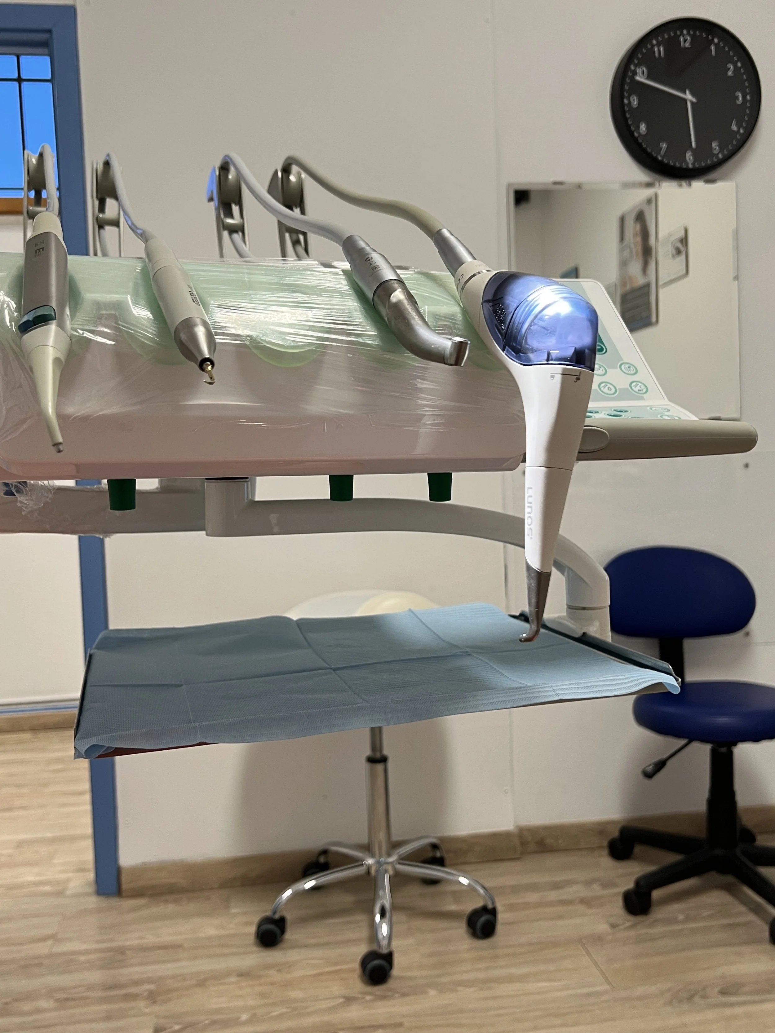 Attrezzature dentistiche in uno studio dentistico, tra cui uno strumento a risonanza, un manipolo e un'unità dentale, con sedie e pareti bianche.