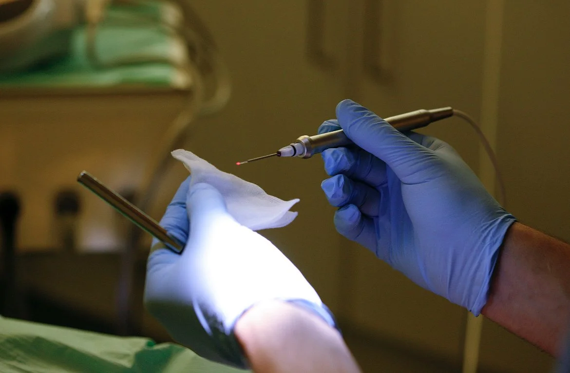 Mani con guanti Blu che maneggia un ago e una striscia di tessuto in un ambiente medico.