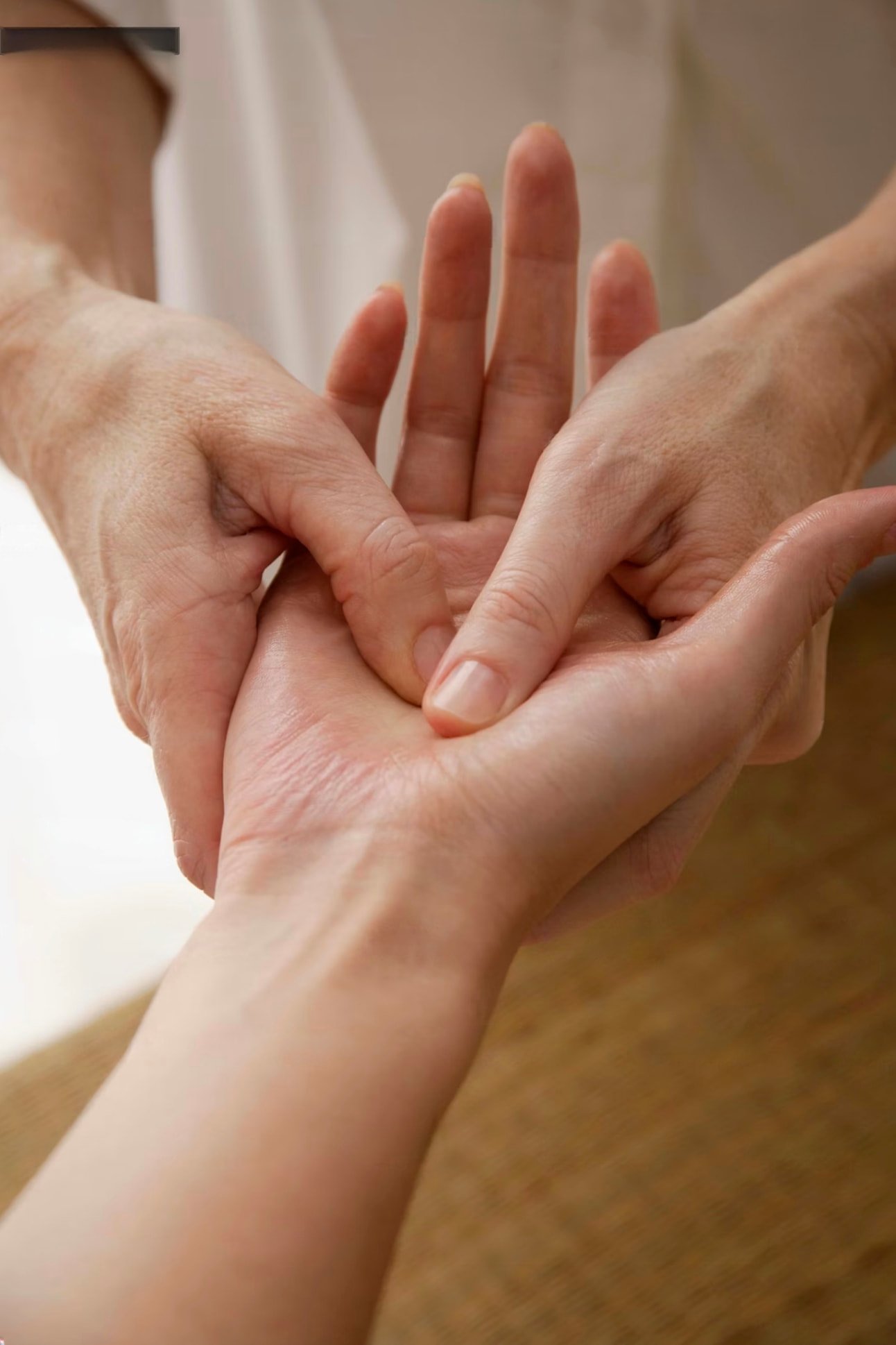Close-up of one person gently holding and touching another person's hand and wrist, showing a caring gesture.