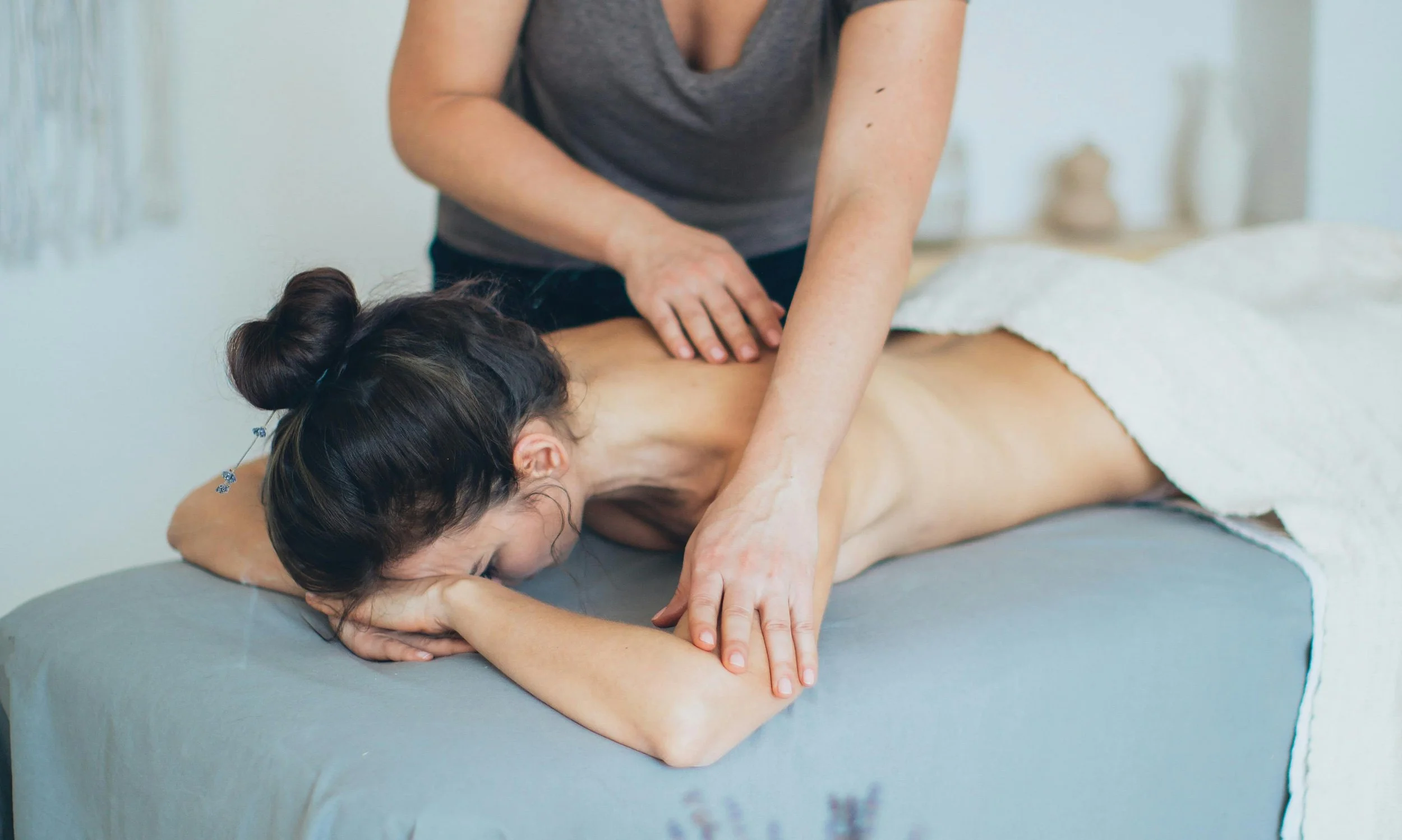 A woman receiving a massage on her back from a massage therapist in a spa setting.