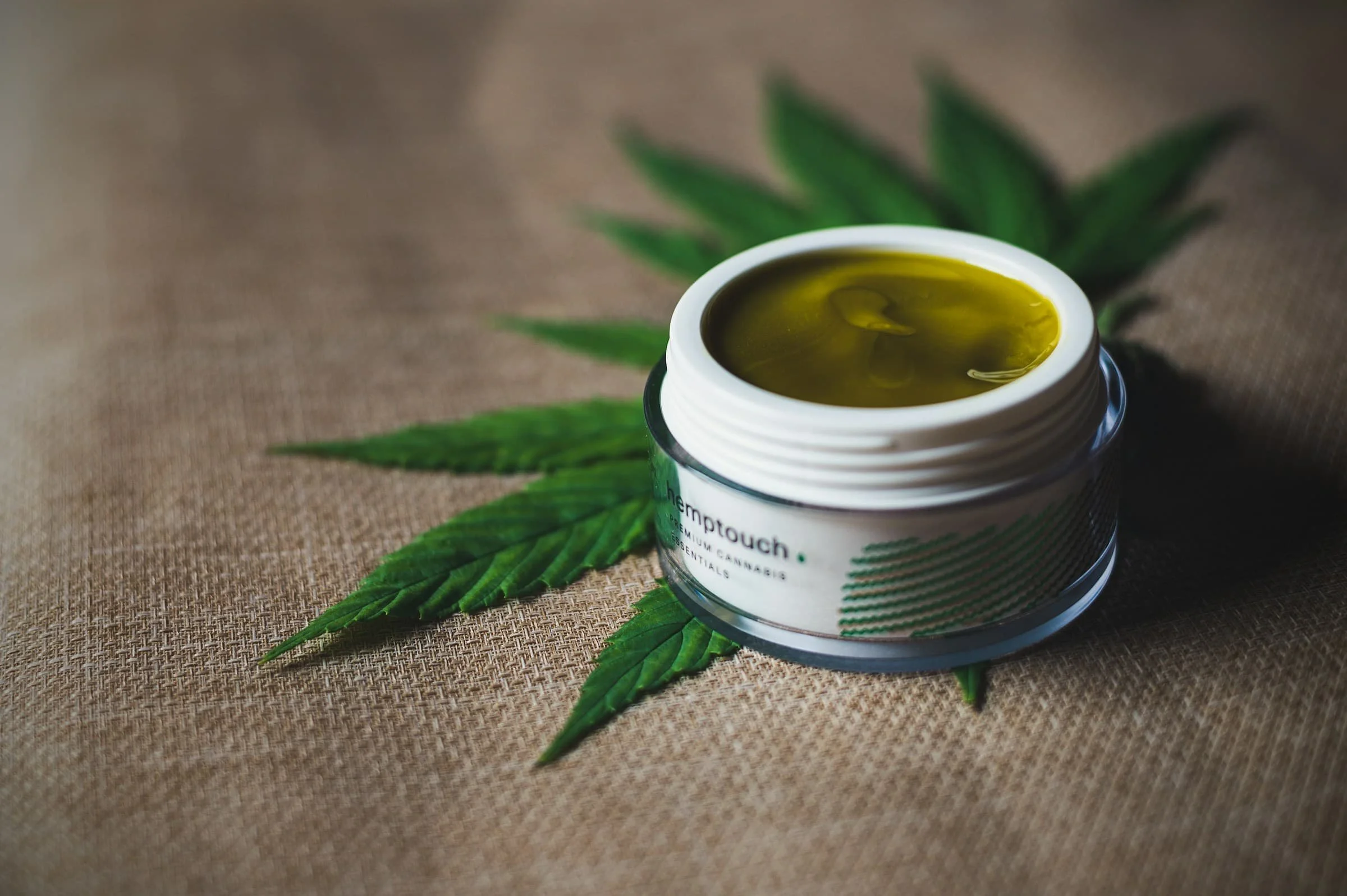 Open container of CBD cannabis extract placed on a paper mat with cannabis leaves underneath.
