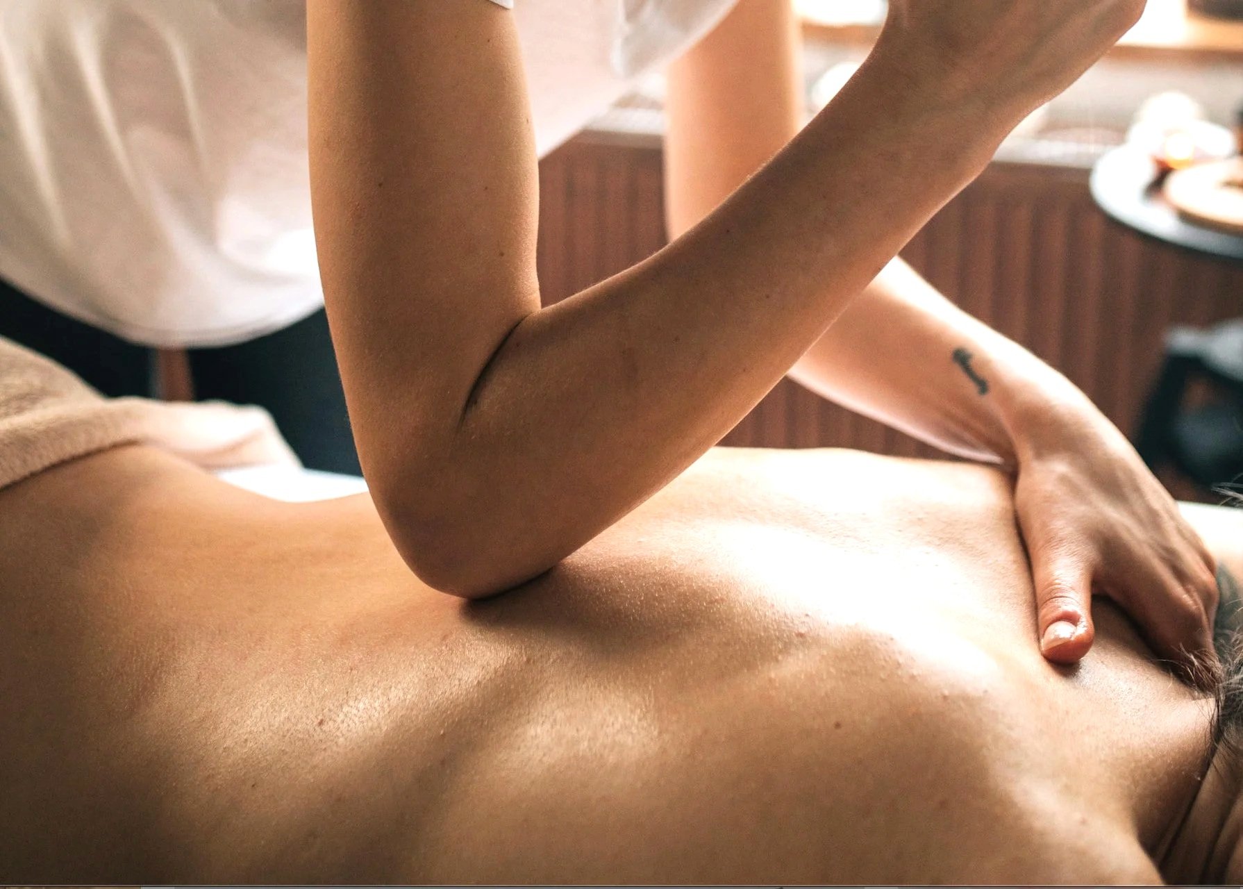 Close-up of a person's hand and forearm receiving a massage on their back in a warm-lit room.