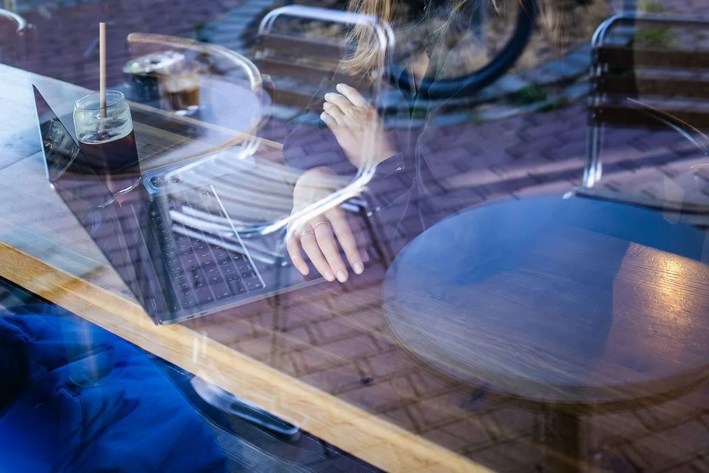 Jana Tasche arbeitet konzentriert am Laptop durch Fenster fotografiert mit Reflexion