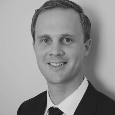Black and white headshot of a man in a suit and tie, smiling.