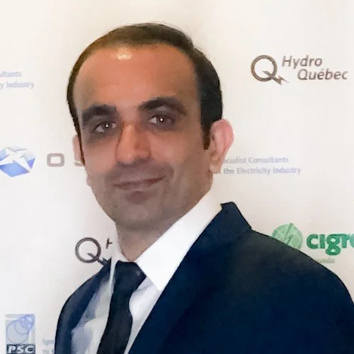 A man in a dark suit and tie standing in front of a backdrop with logos for Hydro Quebec and other organizations.