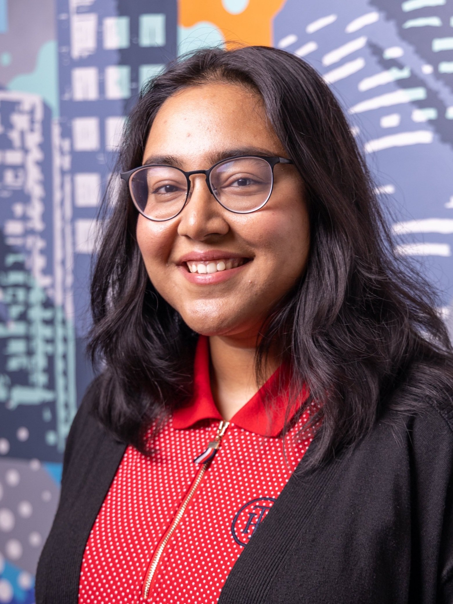 A woman with glasses smiling in front of a colorful mural.