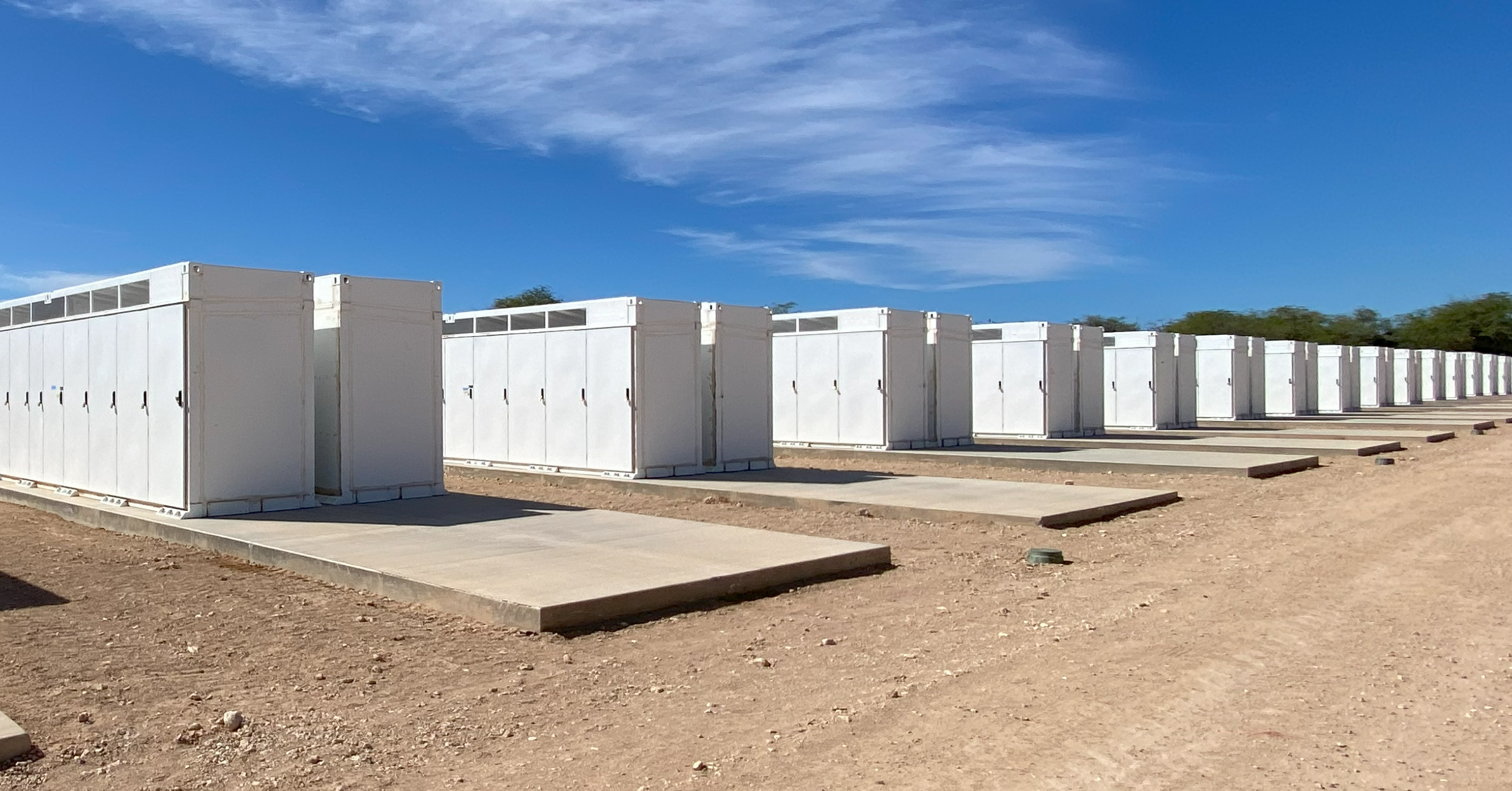 Row of white BESS solar battery storage on a dirt ground under a blue sky with some clouds. Revamp Engineering Hawaii BESS solar storage project.