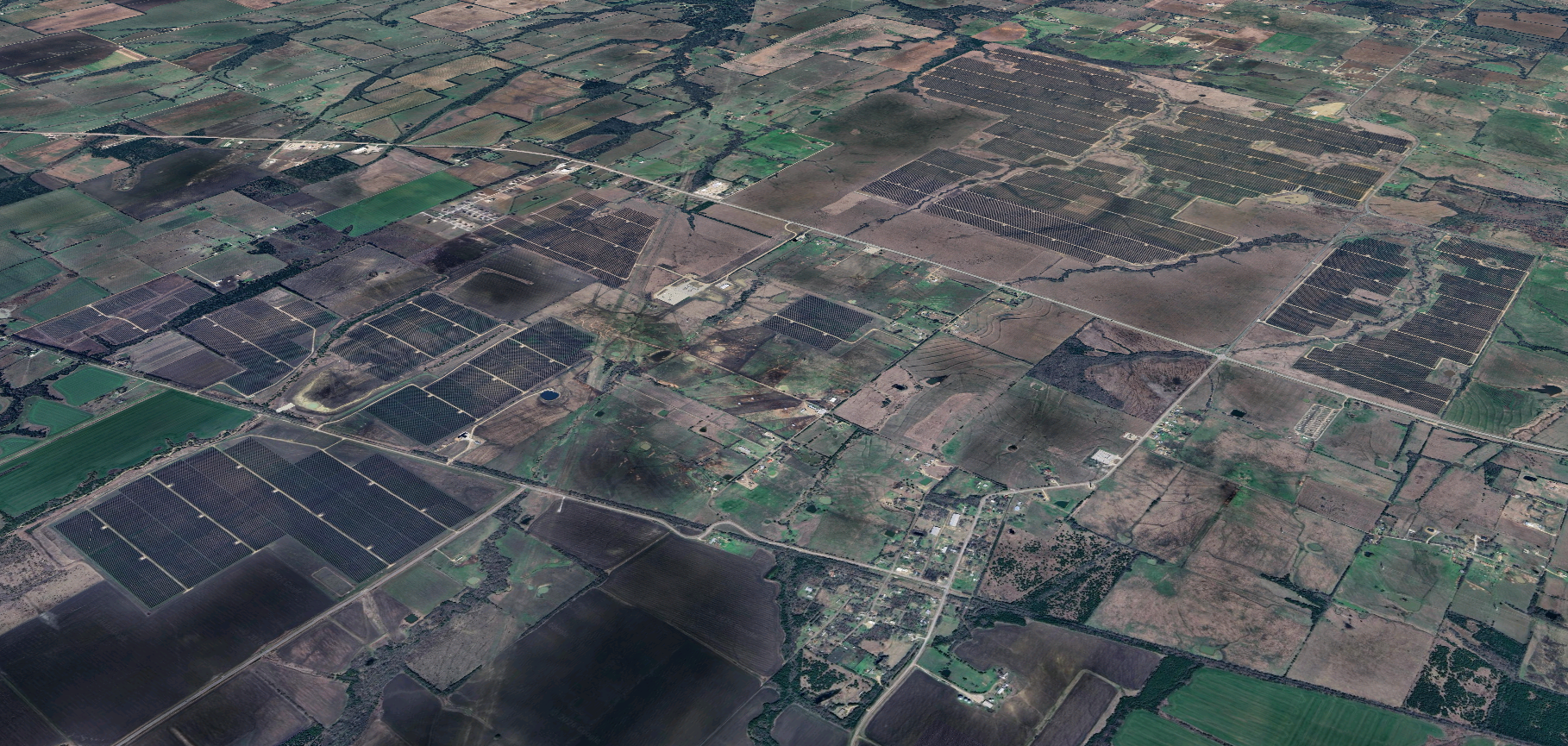 Aerial view of rural farmland, showing green fields, solar panels, roads, and scattered buildings over a patchwork landscape.