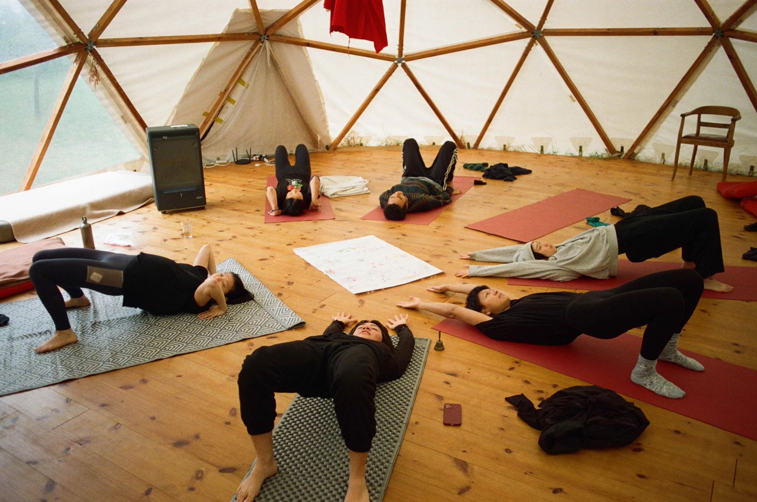 photo of Sonia leading a group of participant during a group yoga session. Everyone is stretched out in a circle on the floor with their eyes closed.