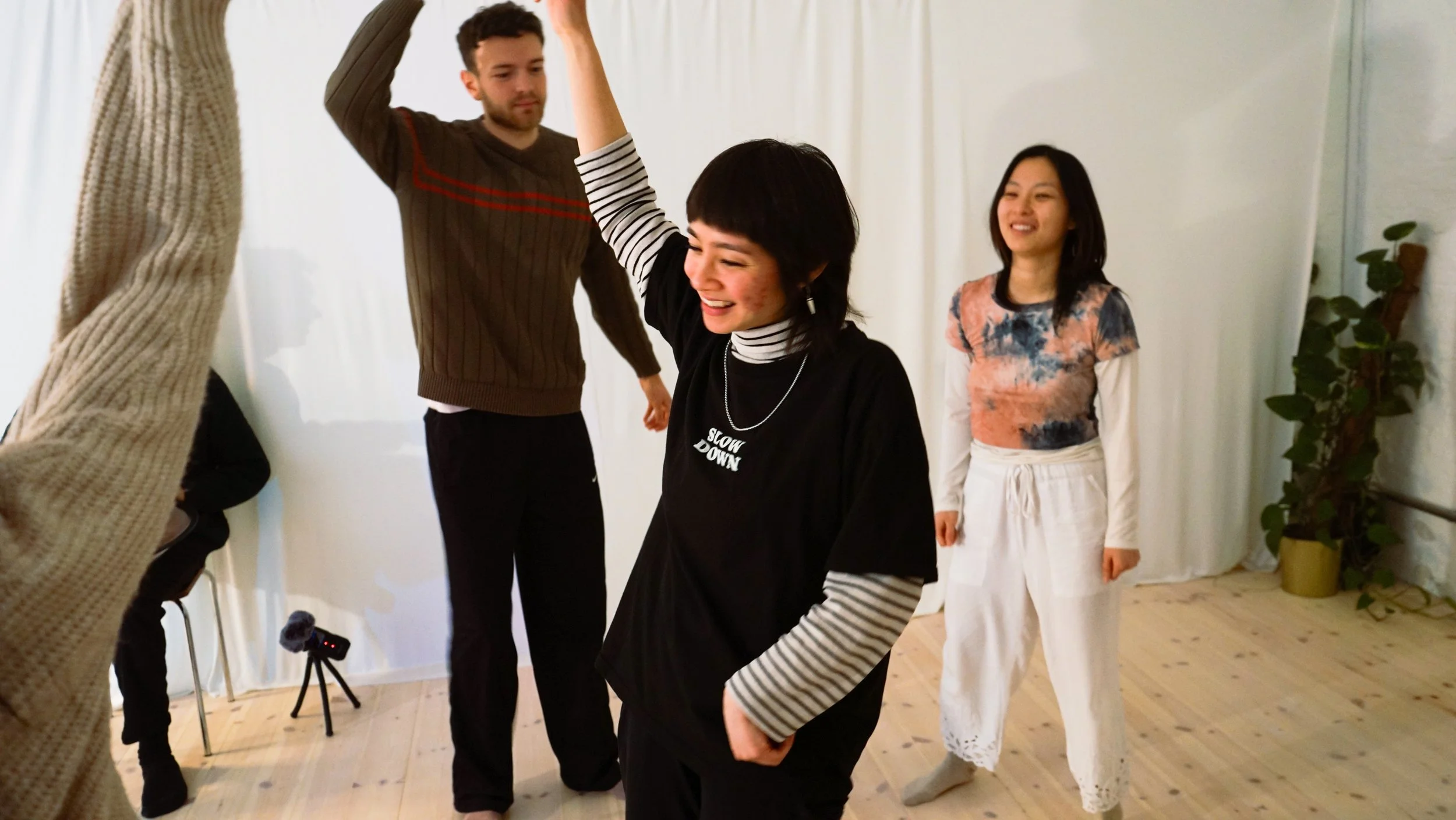 A photo of Sonia leading a somatic movement session in the foreground with two participants moving and smiling in the background.