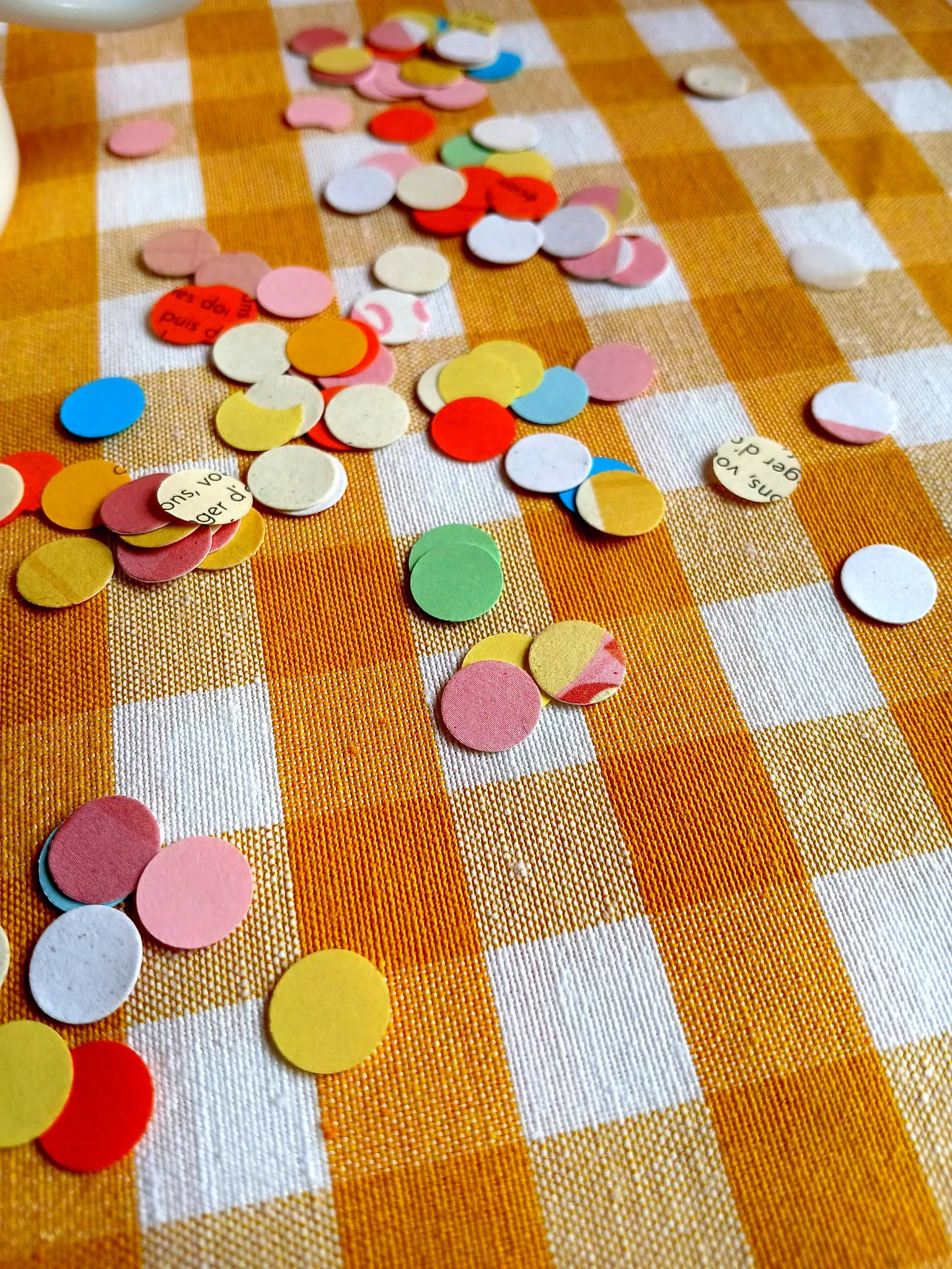 Confettis colorés dispersés sur un tissu à motif à carreaux orange et blanc.