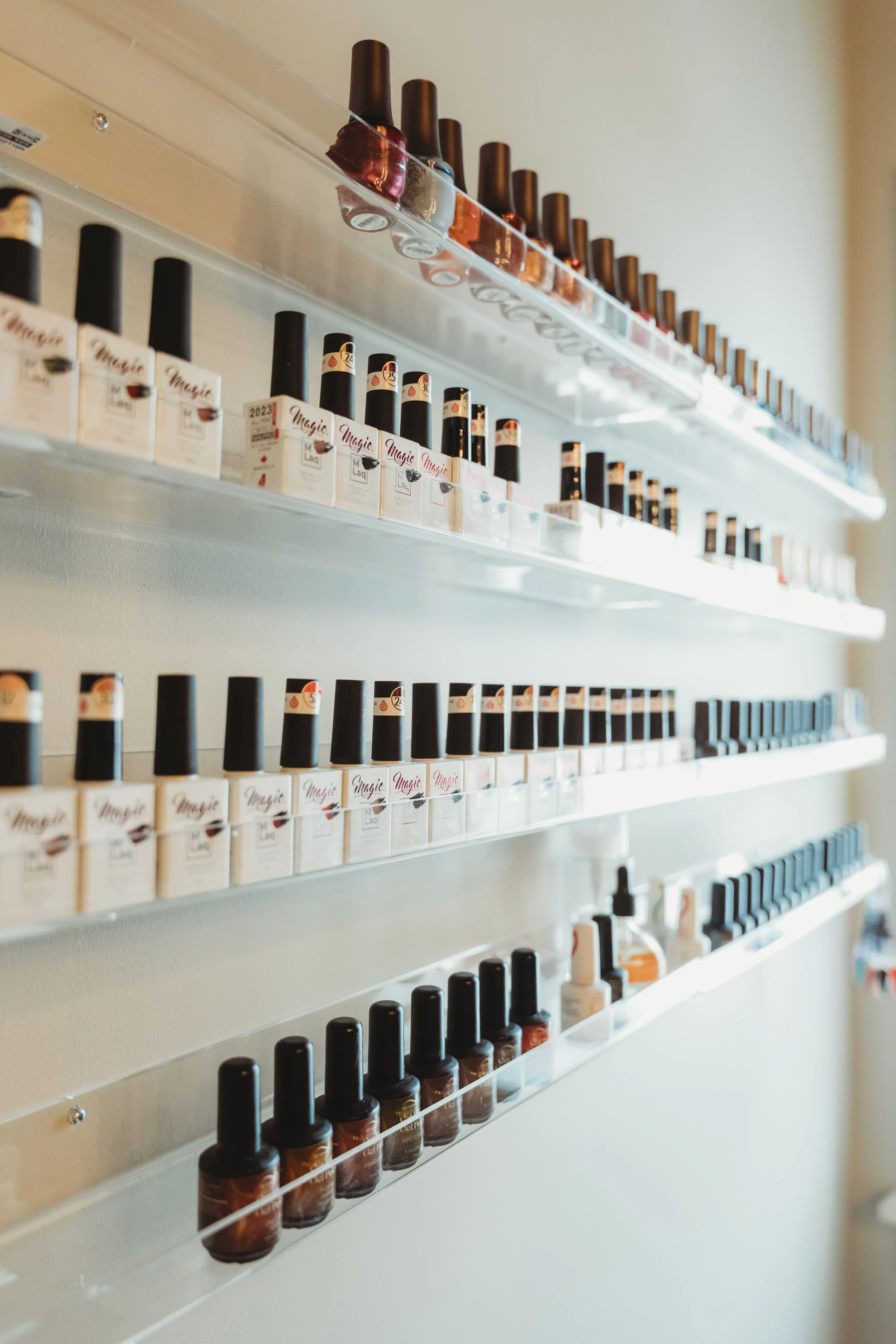 Nail polish bottles displayed on clear wall-mounted shelves, with various shades and brands.