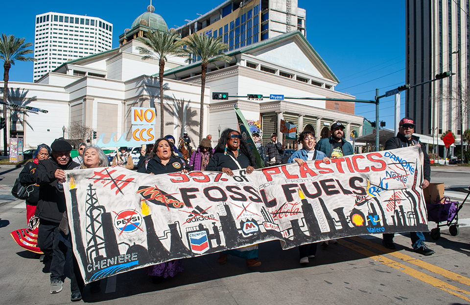 A group of people march while holding signs and a large banner.