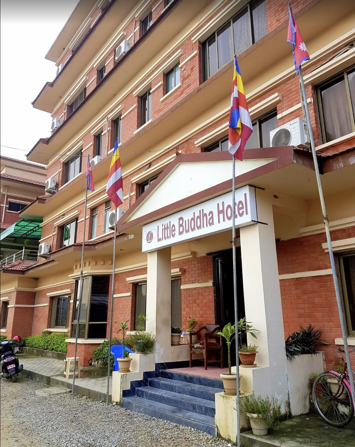 Exterior view of Little Buddha Hotel, a multi-story brick building with balconies, flags, and a small entrance with steps and potted plants. Wildlife expedition and phot safari with Wild Selection Tours.