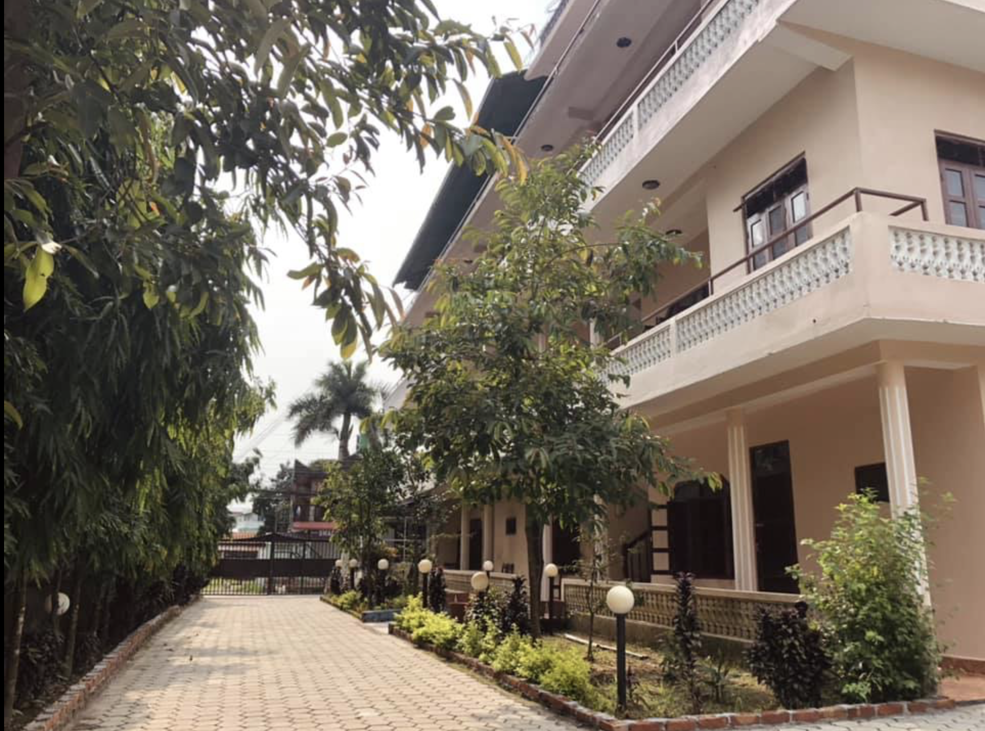 Exterior view of a multi-story residential building with balconies, surrounded by landscaped garden with small trees, bushes, and pathway lined with lampposts. Wildlife expedition and phot safari with Wild Selection Tours.