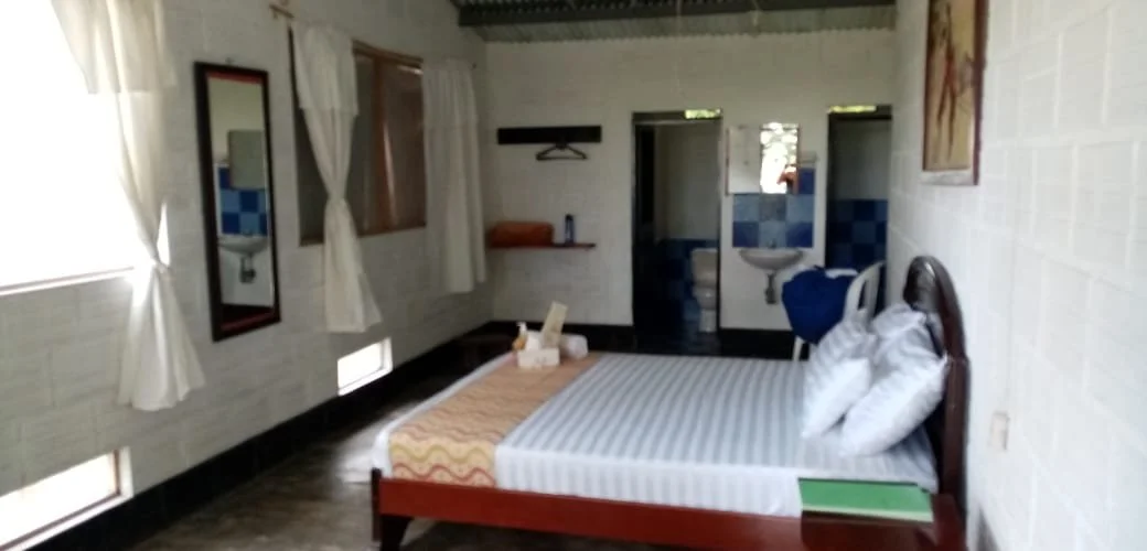 Hotel room with a bed, mirror, window with curtains, and a small bathroom area in the background.